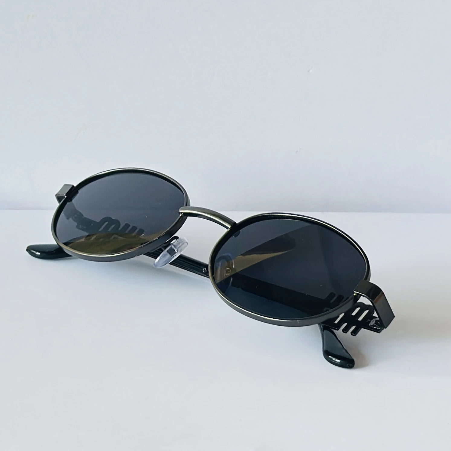 sunglasses featuring a distinct black oval frame and small logo detailing on the lenses