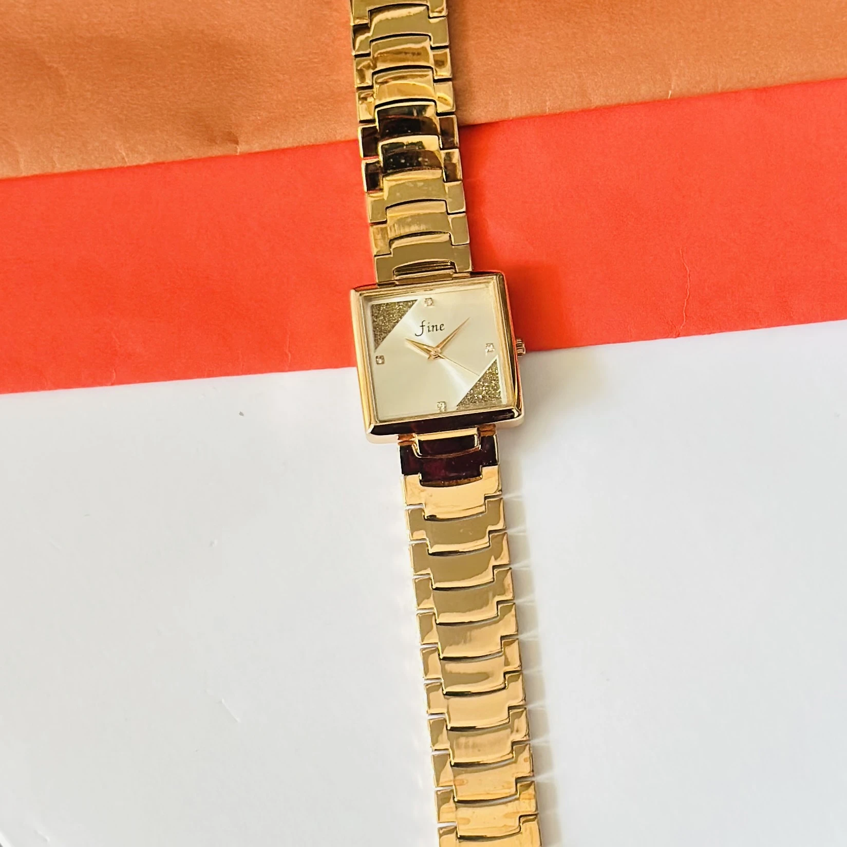 Gold -tone analog watch with a square dial and a metal strap.