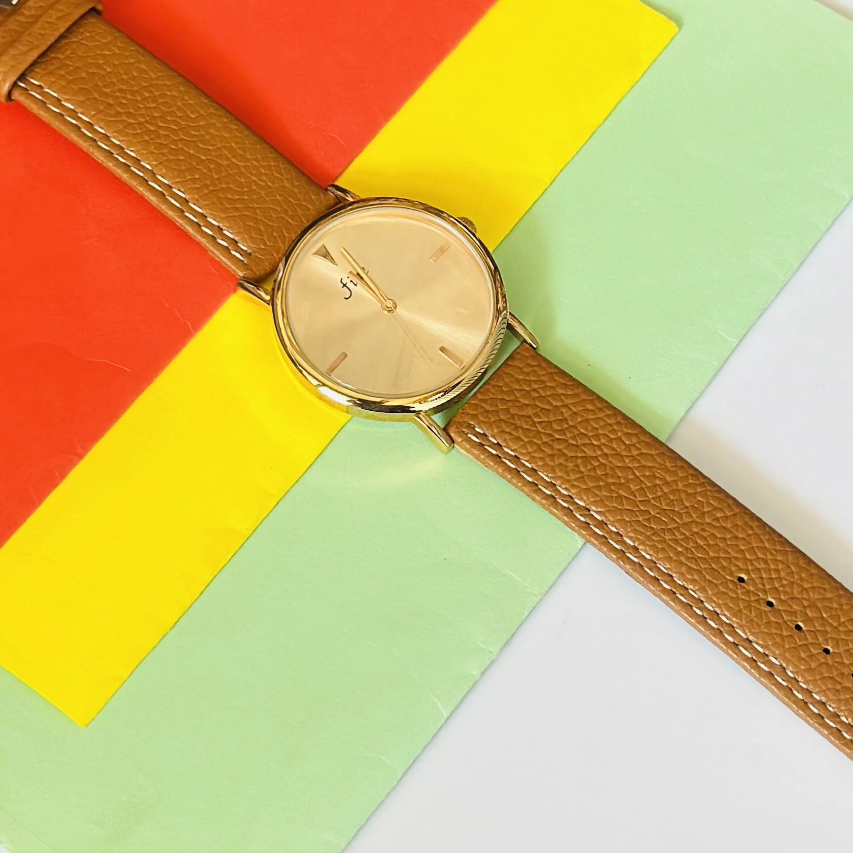 analog wristwatch with a gold-tone case and a brown leather strap.