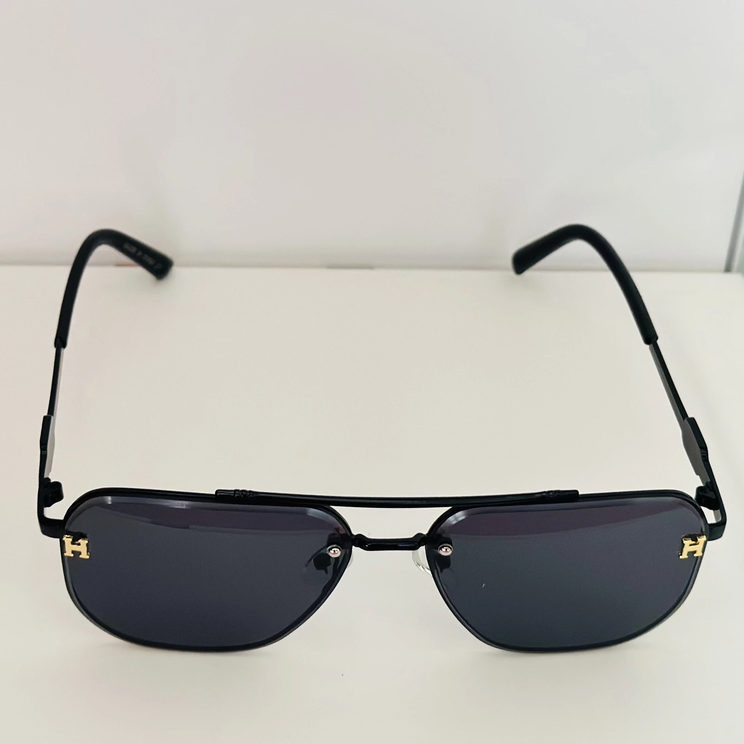 Black rimless aviator sunglasses with gold-tone "H" emblems on the temples.