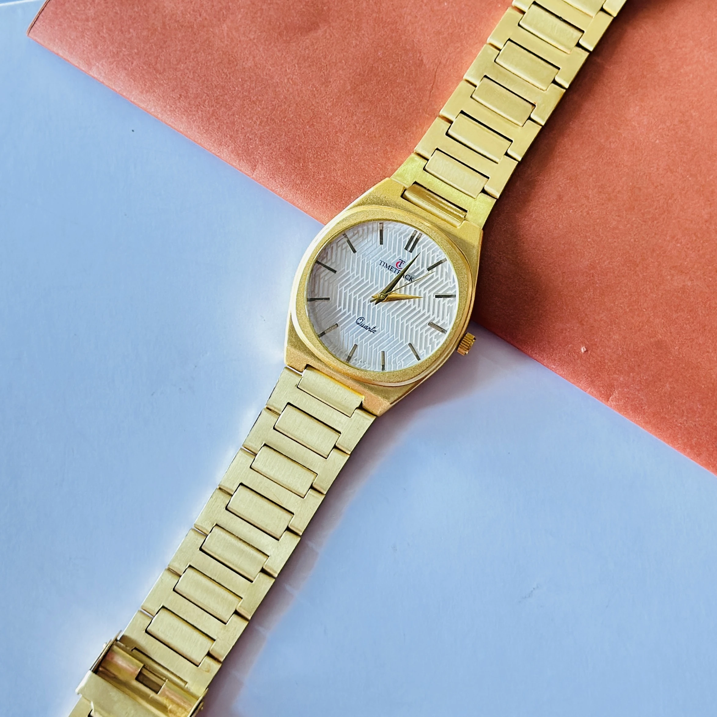Timetrack quartz analog watch with a gold-plated stainless steel band and a white patterned dial.