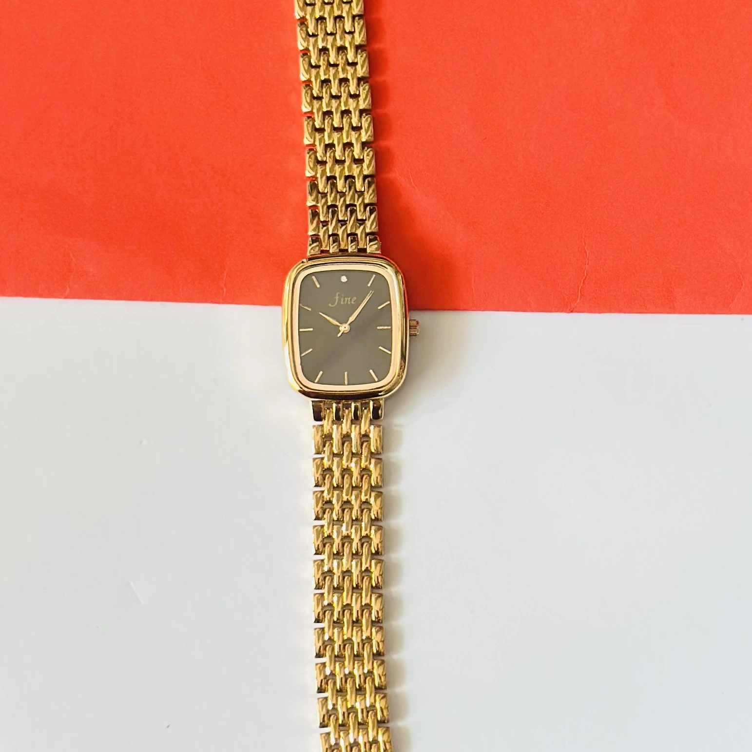 Gold tone analog watch with a square dial and a metal strap.
