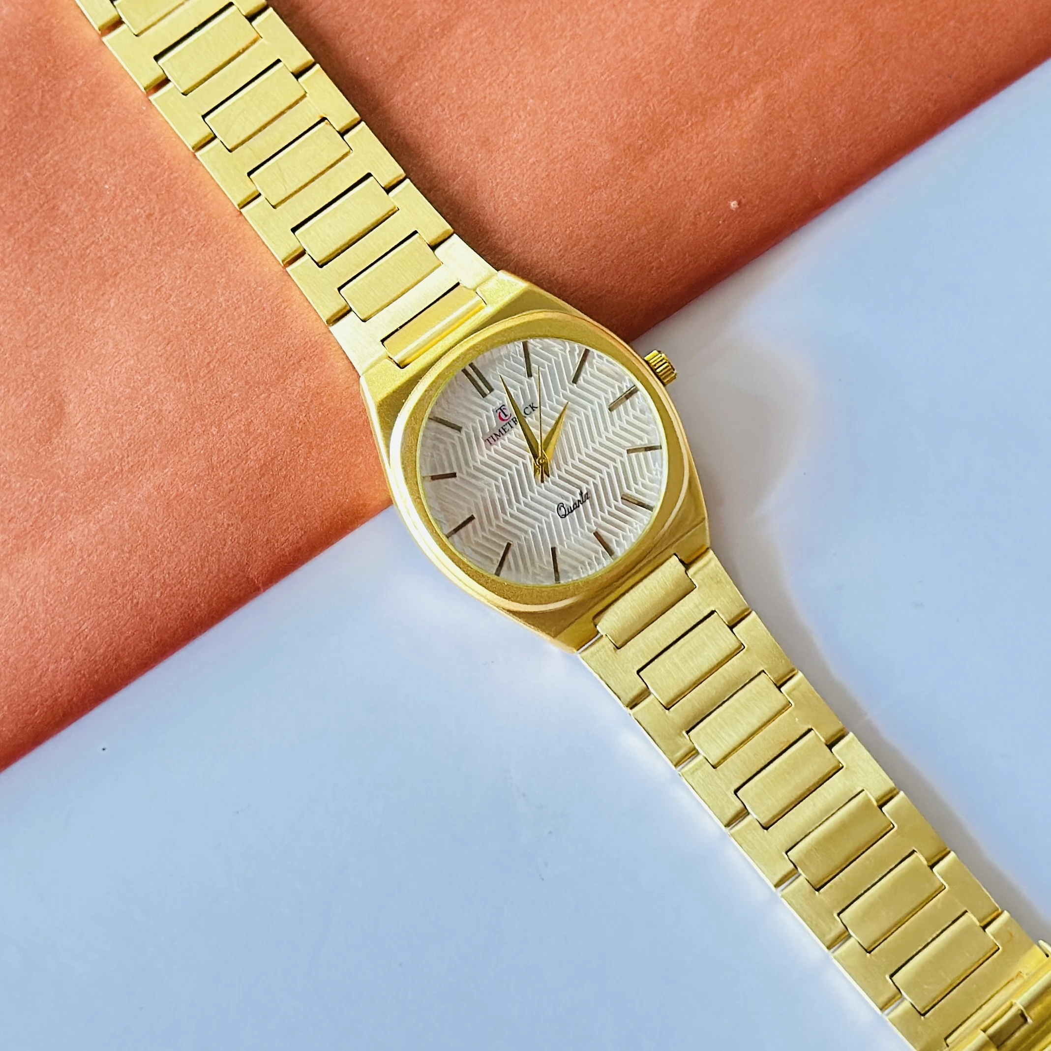 Timetrack quartz analog watch with a gold-plated stainless steel band and a white patterned dial.