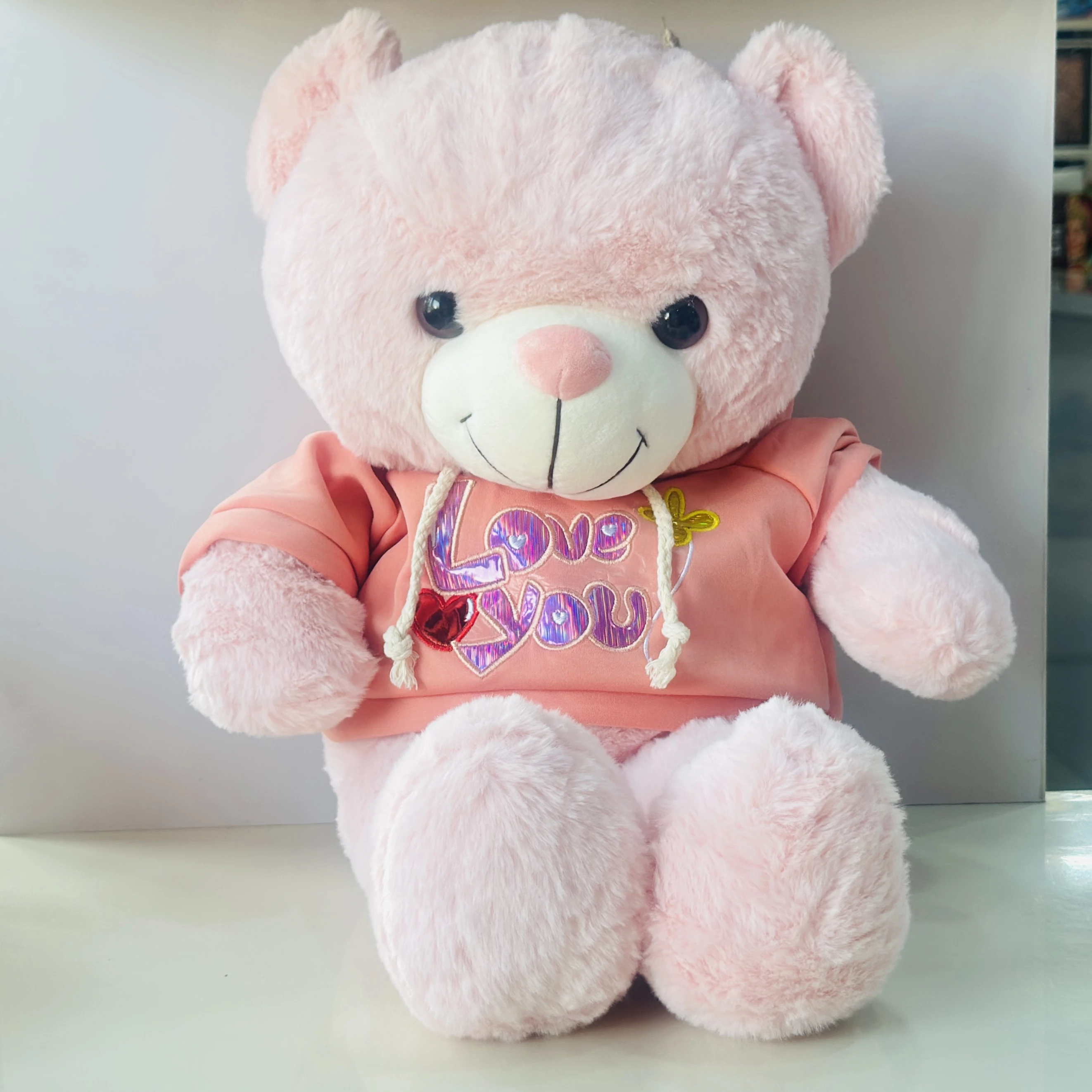 soft plush teddy bear toy wearing a pink hoodie with "I Love You" text.
