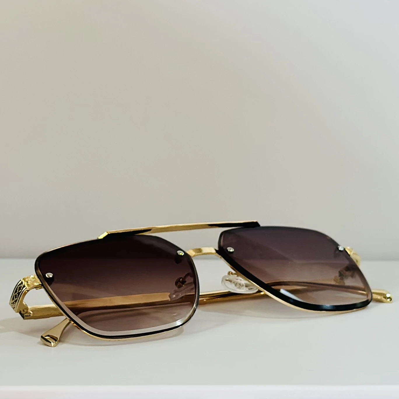 pair of rimless gradient brown aviator sunglasses with a gold metal frame and ornate side details.