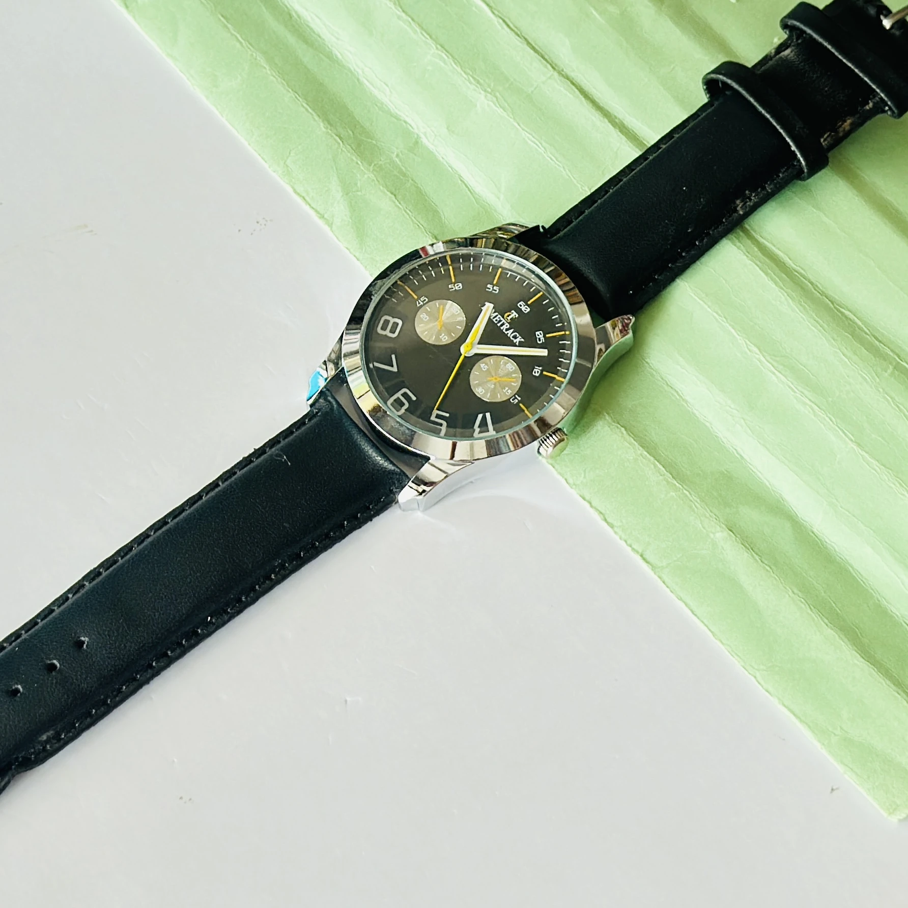 Metrack brand analog watch featuring a black dial and a black leather strap.