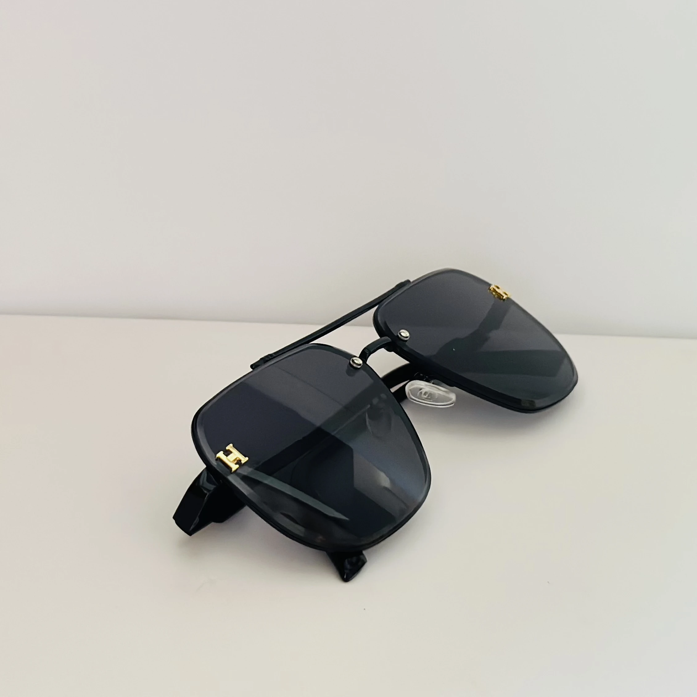Black rimless aviator sunglasses with gold-tone "H" emblems on the temples.