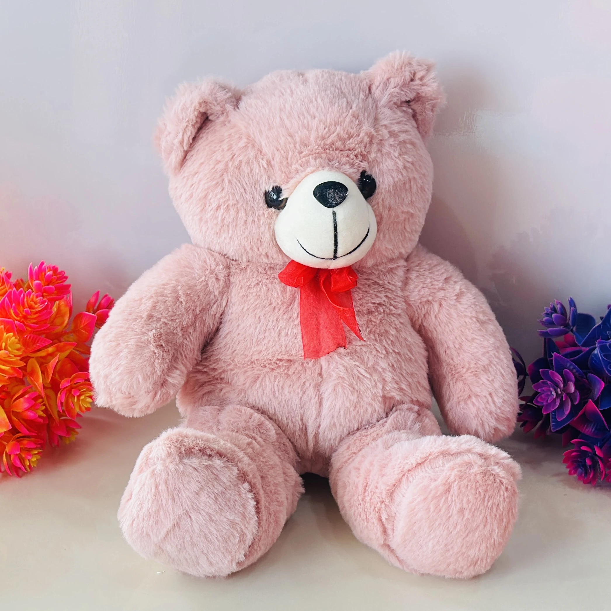 Large pink stuffed teddy bear with a red bow