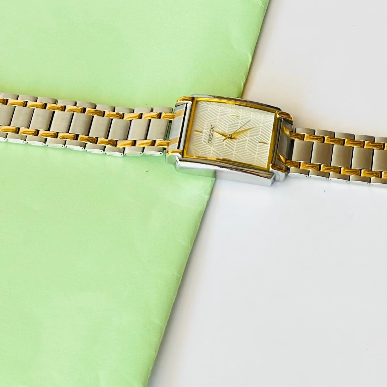 Crescent analog watch with a rectangular case and a two-tone (silver and gold) metal bracelet.