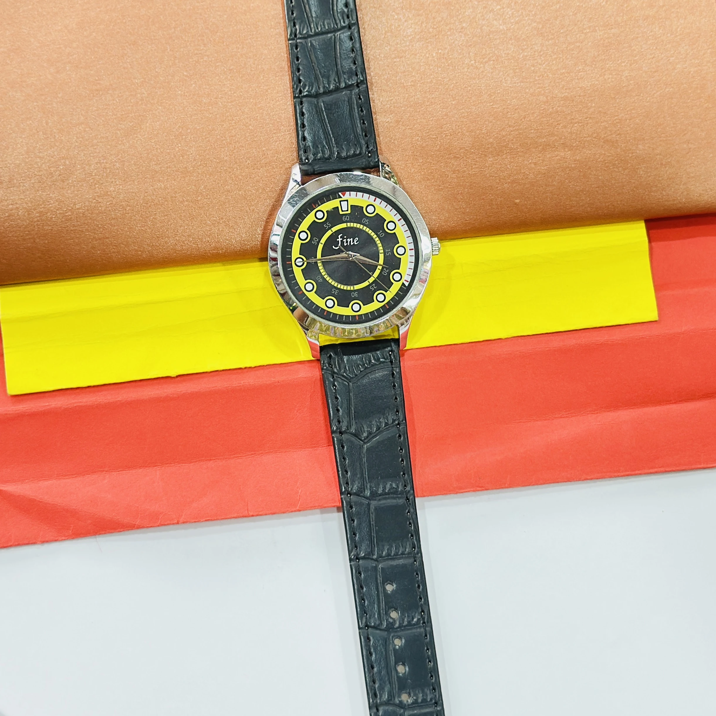 Fine" brand wristwatch featuring a black strap and a dial with yellow and black accents.