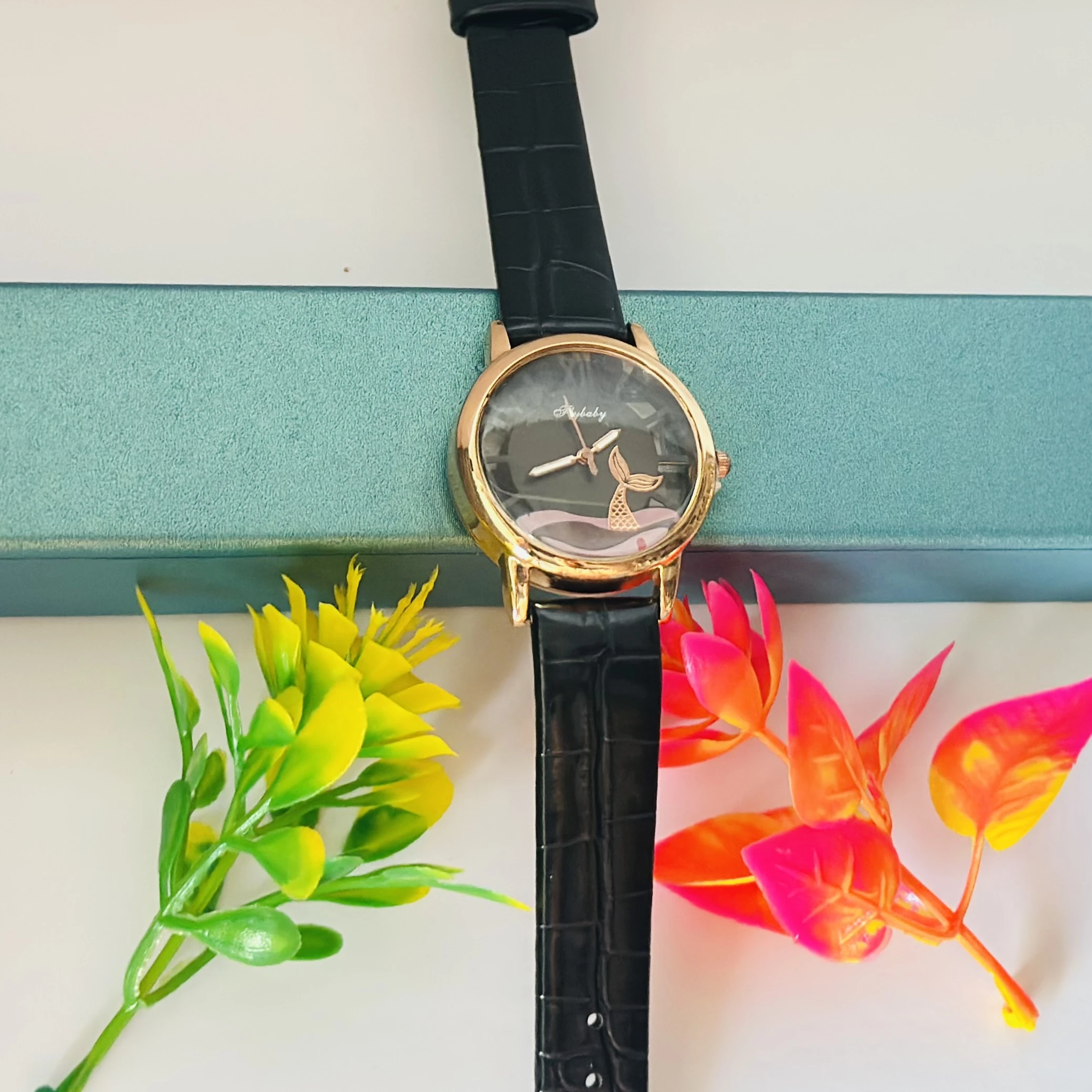 gold-toned analog watch with a black strap and a whale tail design on the dial.
