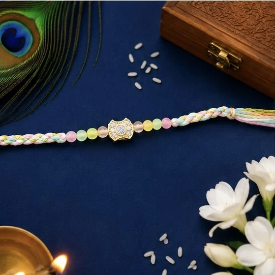 Rakhi bracelet featuring a central golden Kundan-style emblem studded with clear stones.