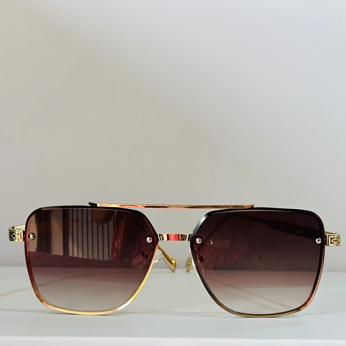pair of rimless gradient brown aviator sunglasses with a gold metal frame and ornate side details.