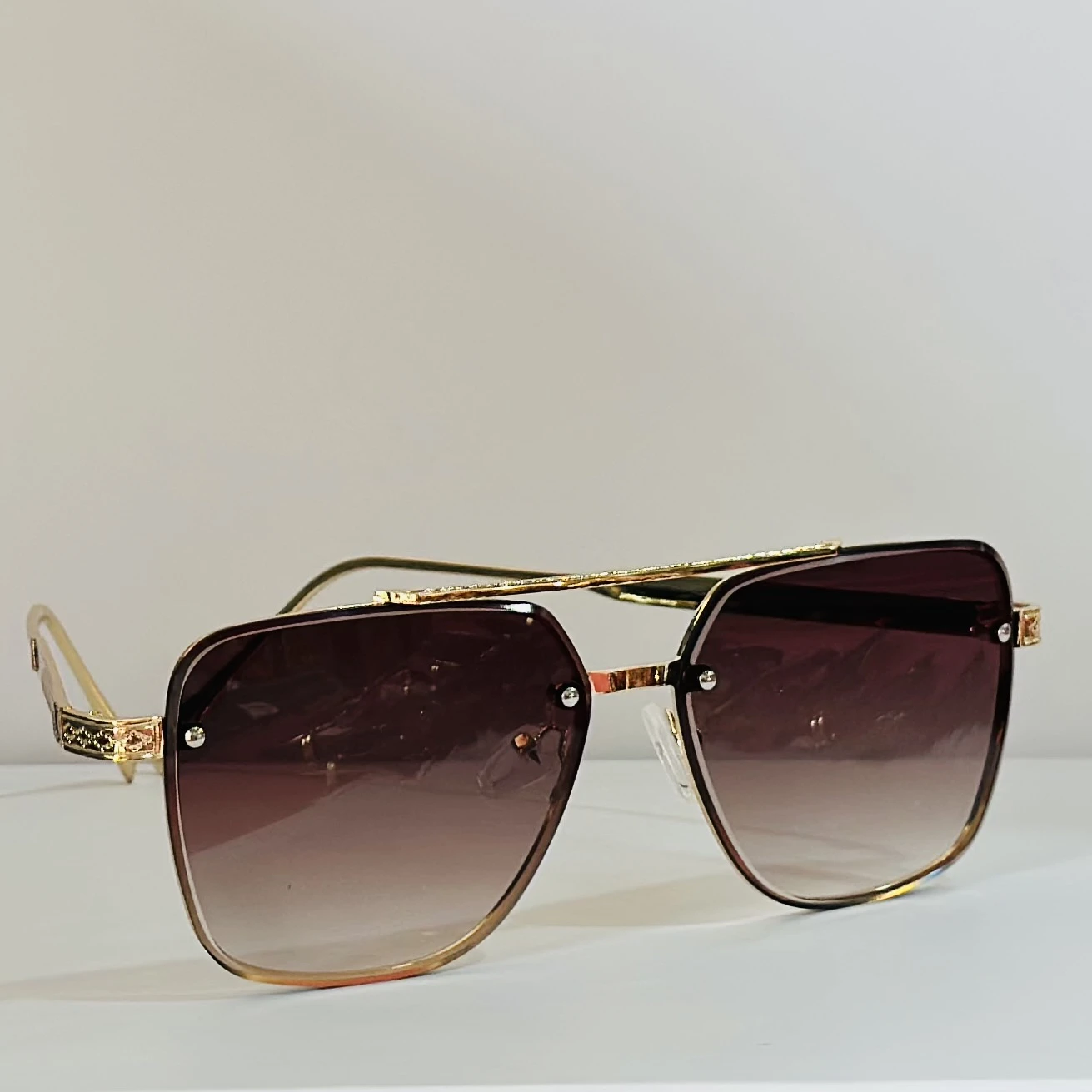 pair of rimless gradient brown aviator sunglasses with a gold metal frame and ornate side details.