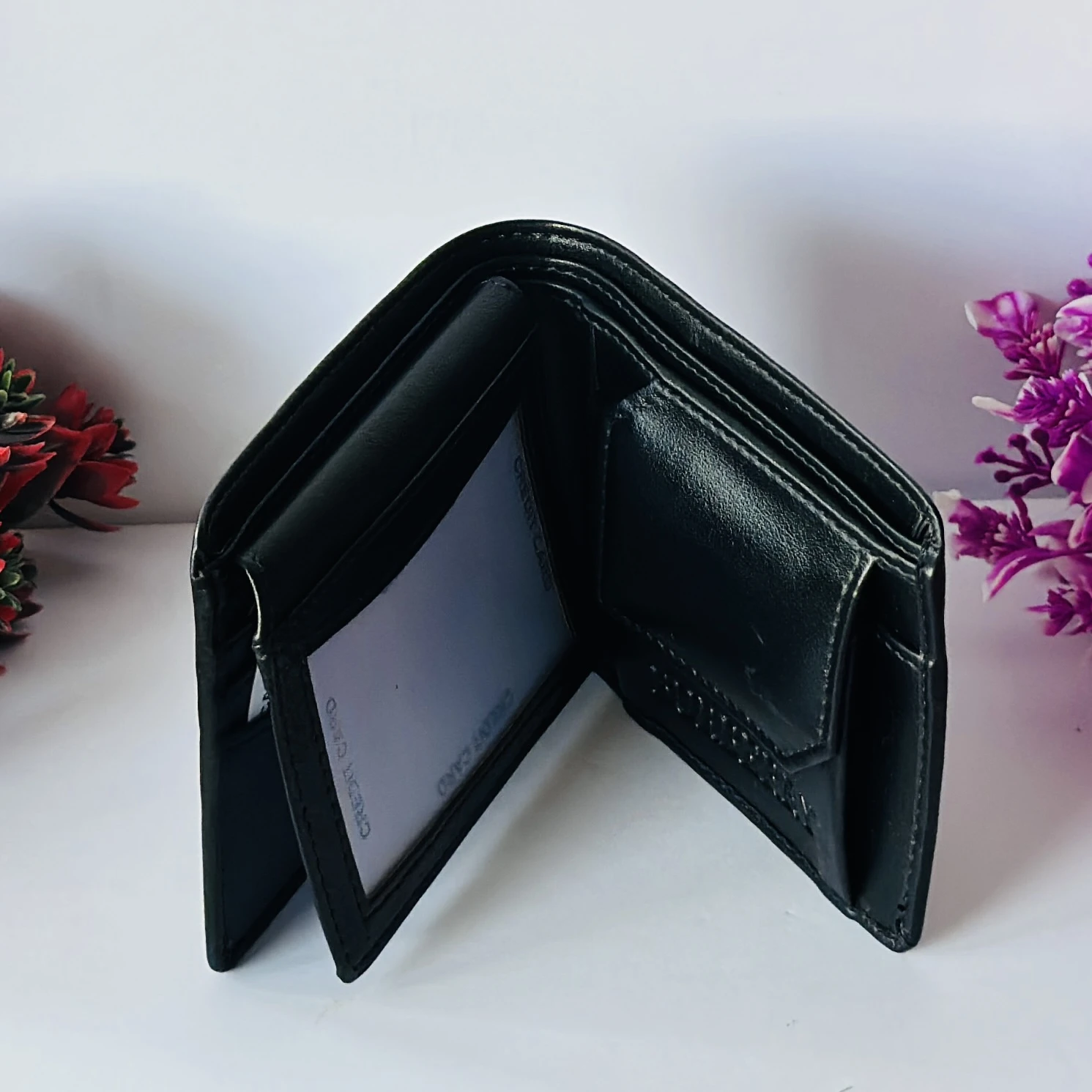 Black bifold leather wallet with a metal logo accent.