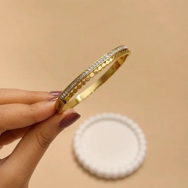 gold-plated stainless steel design with a row of clear stone accents and a scalloped edge.