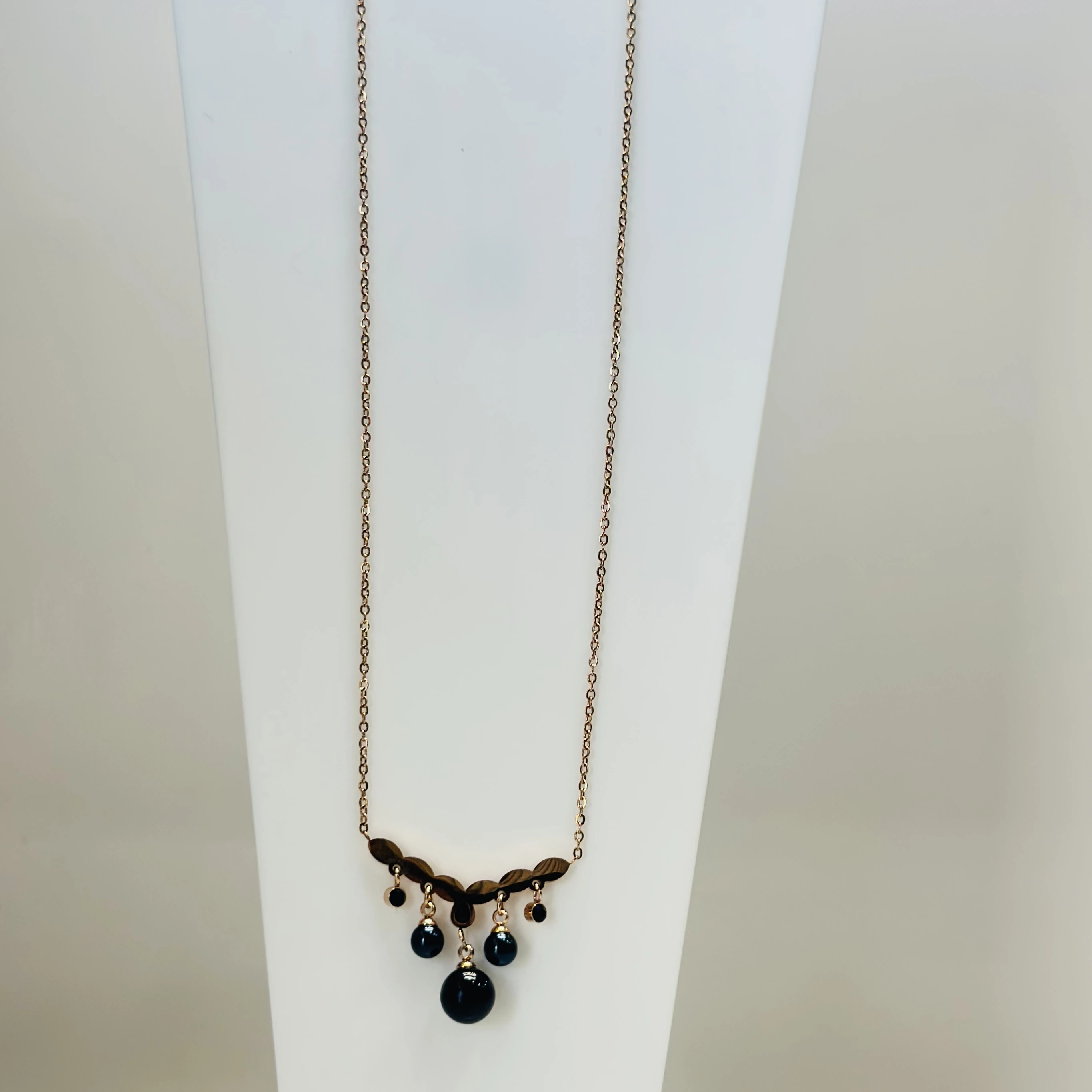 Rose gold-plated pendant necklace with a leaf-motif pendant and black beads.