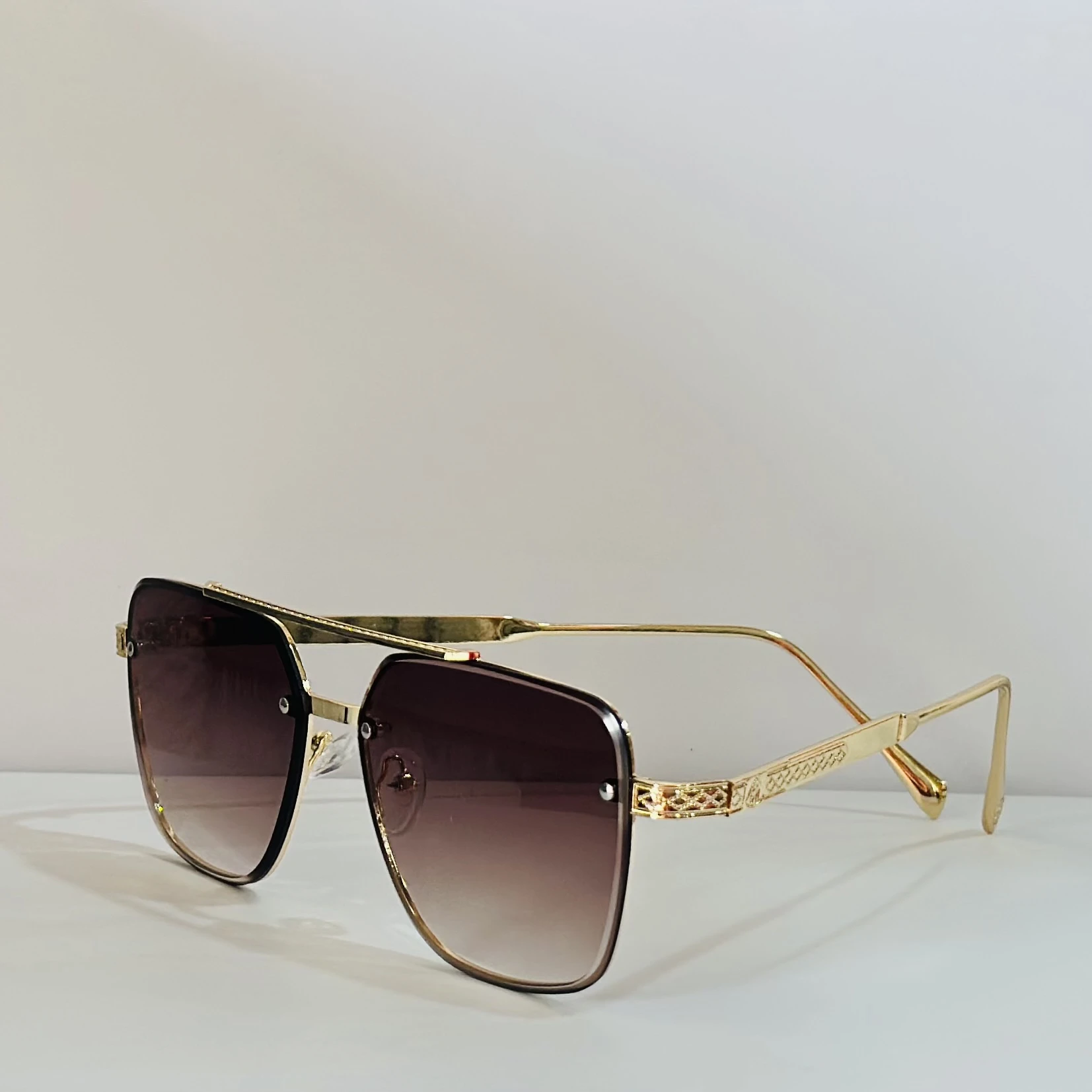 pair of rimless gradient brown aviator sunglasses with a gold metal frame and ornate side details.