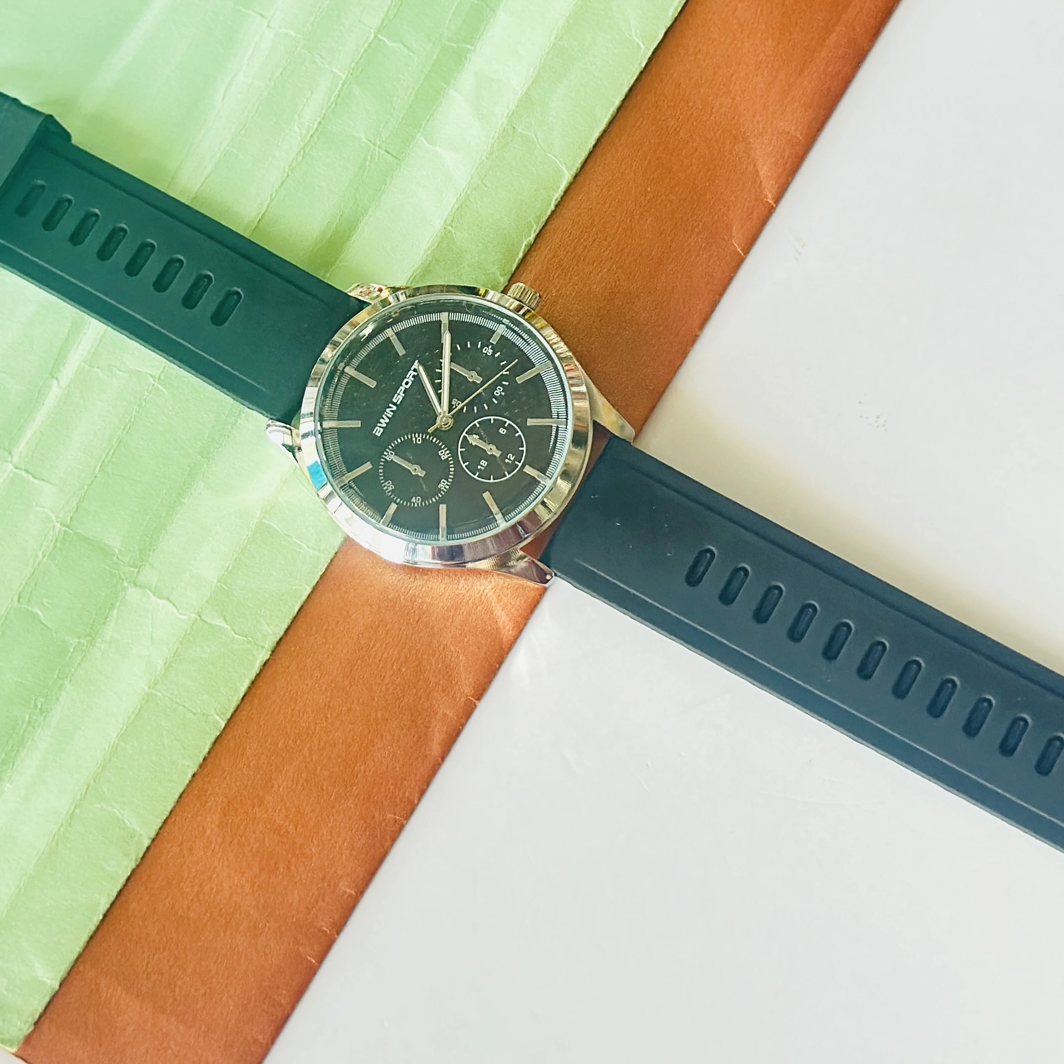 watch features a black dial with sub-dials and a green silicone strap.