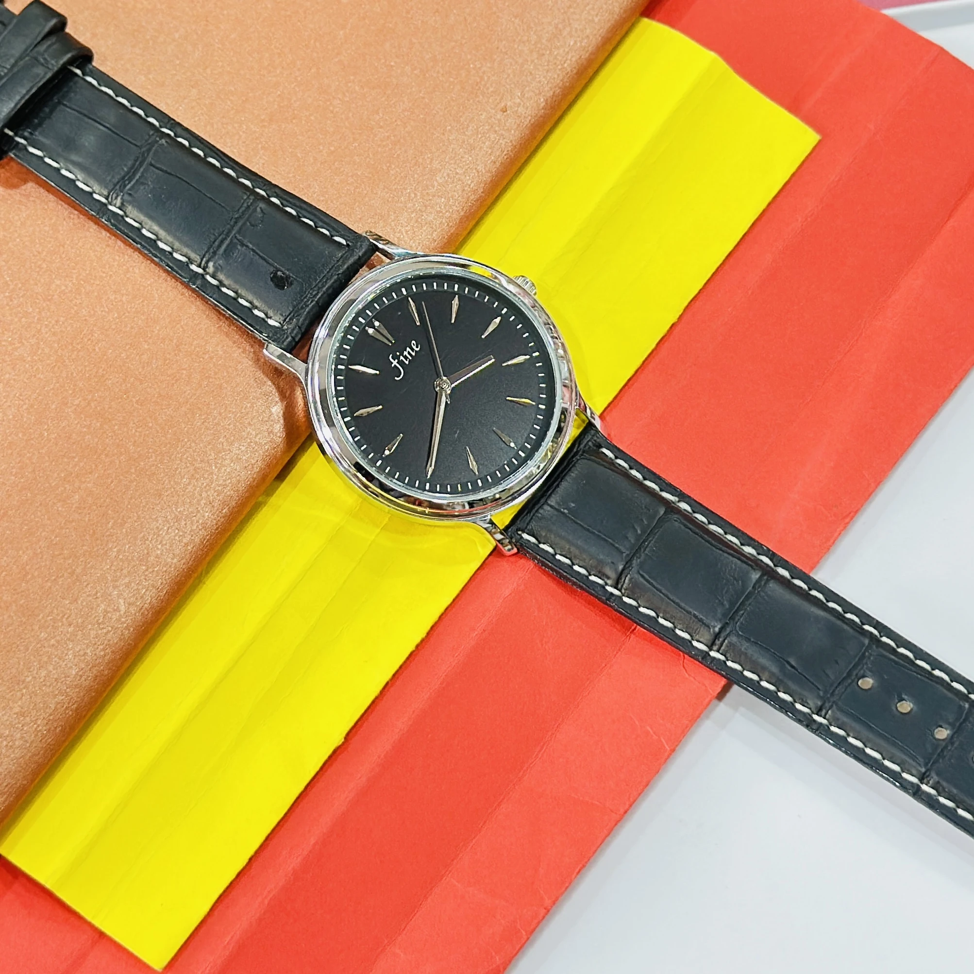 wrist watch featuring a black dial branded as "fine" and a black leather strap.