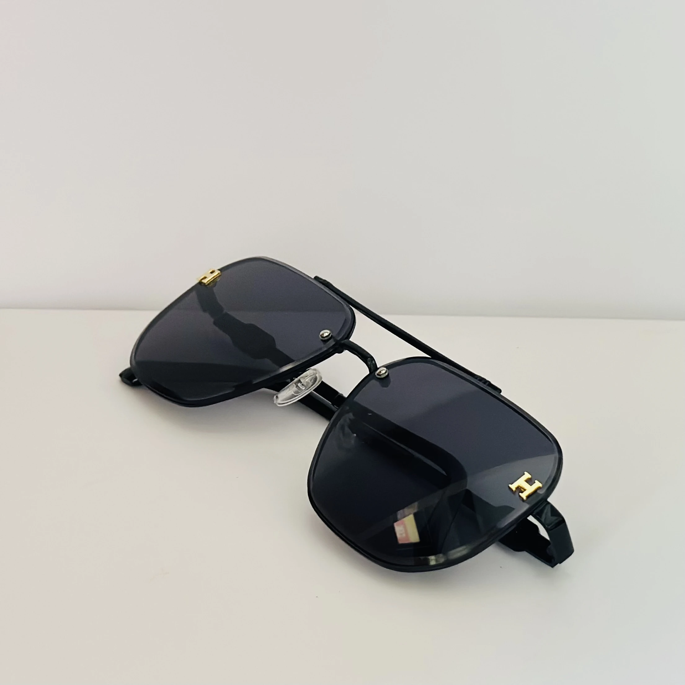 Black rimless aviator sunglasses with gold-tone "H" emblems on the temples.