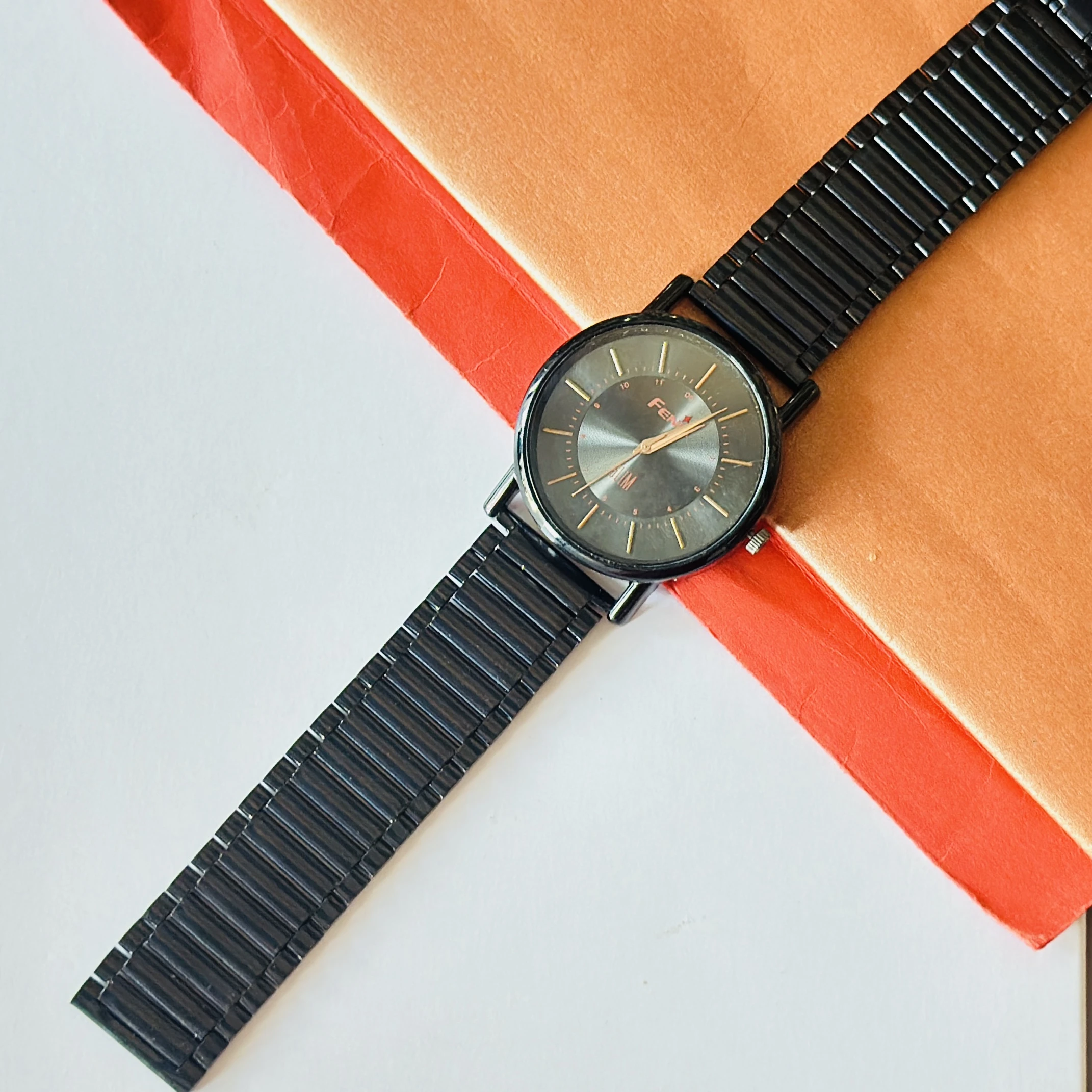 Black metal analog watch with a minimalist design and thin bracelet strap.