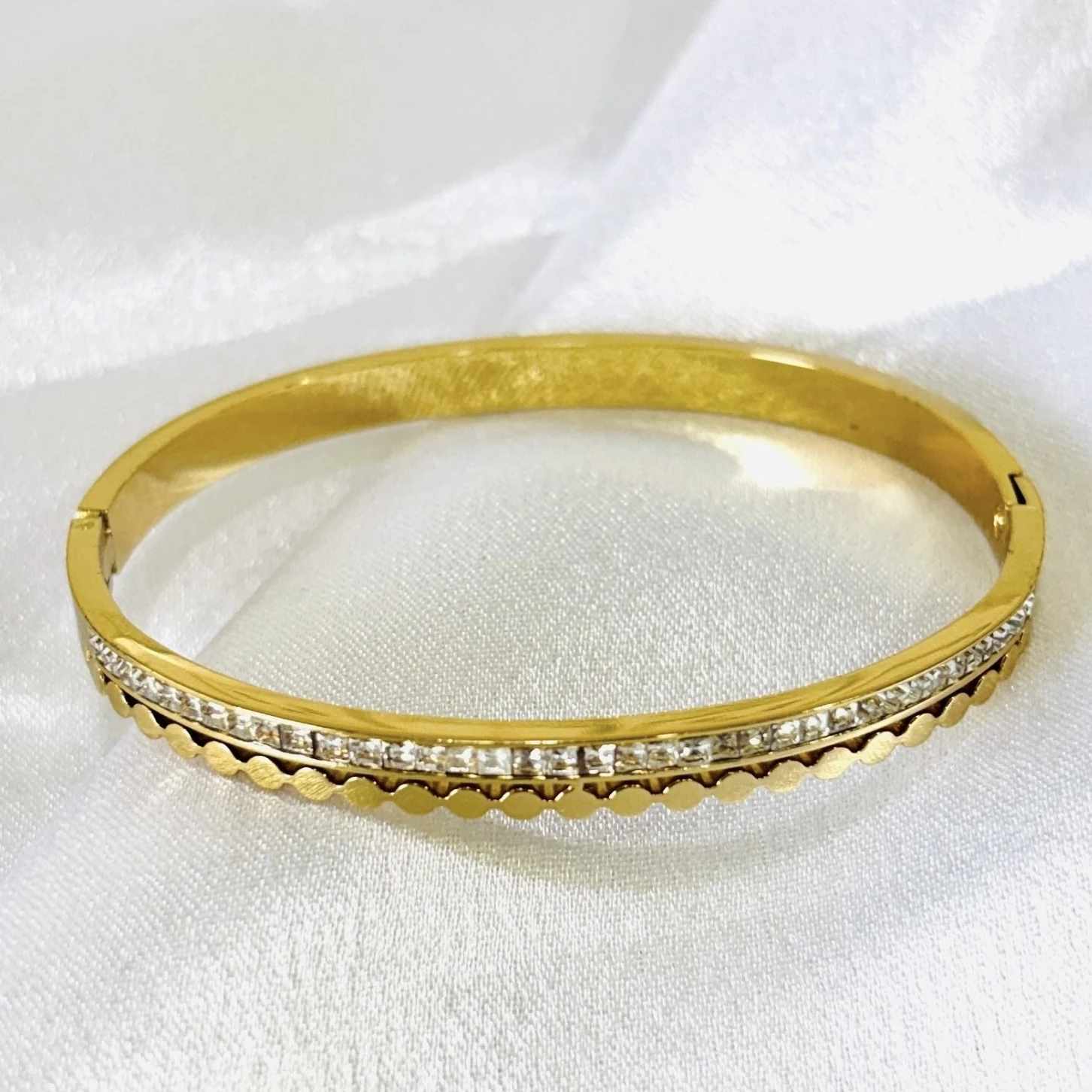 gold-plated stainless steel design with a row of clear stone accents and a scalloped edge.