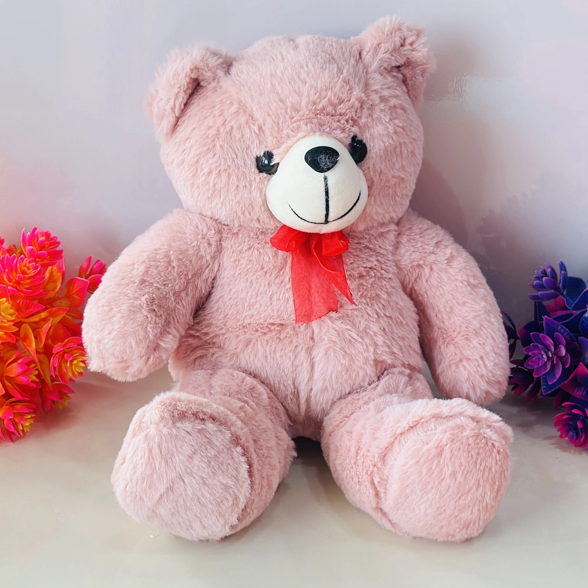 Large pink stuffed teddy bear with a red bow
