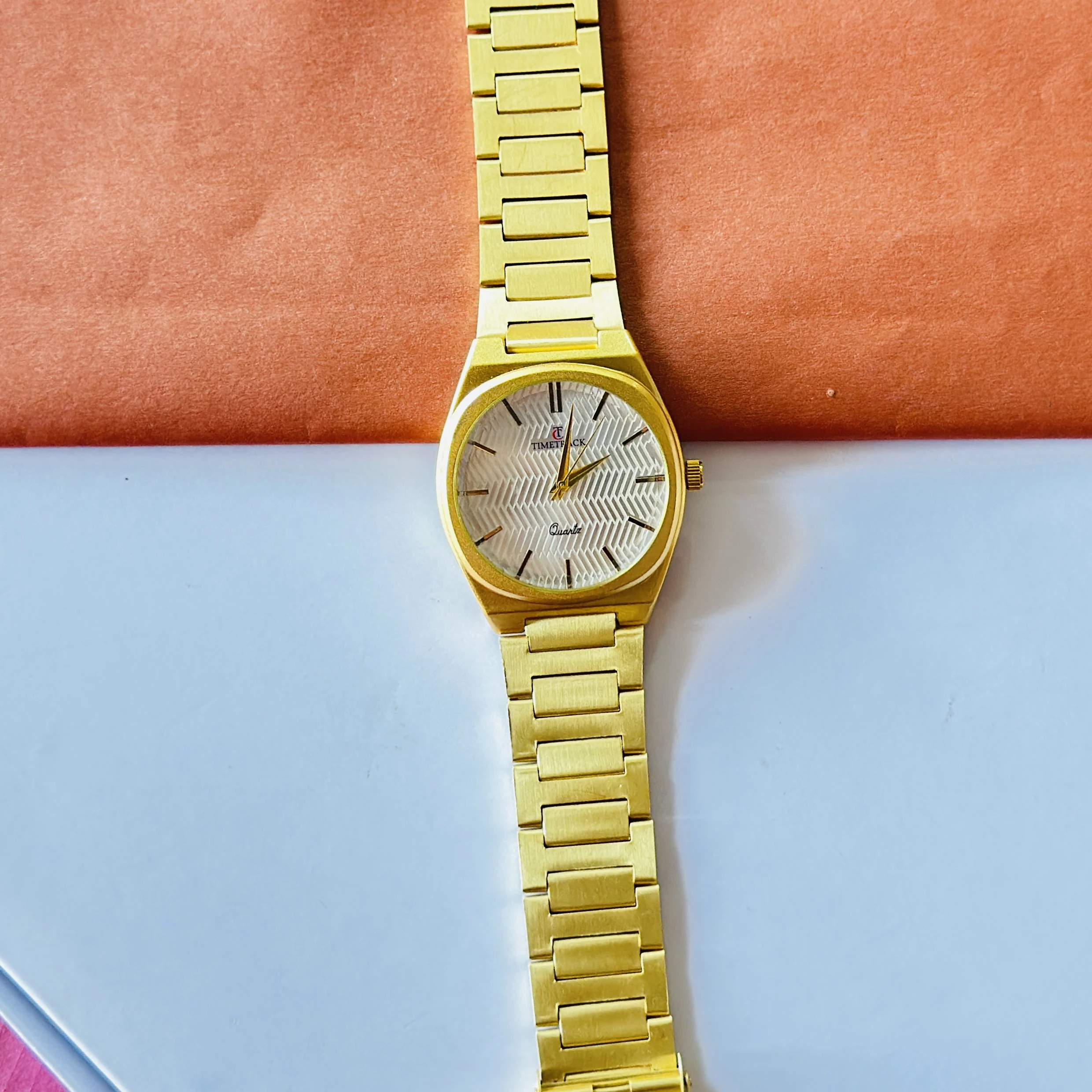 Timetrack quartz analog watch with a gold-plated stainless steel band and a white patterned dial.