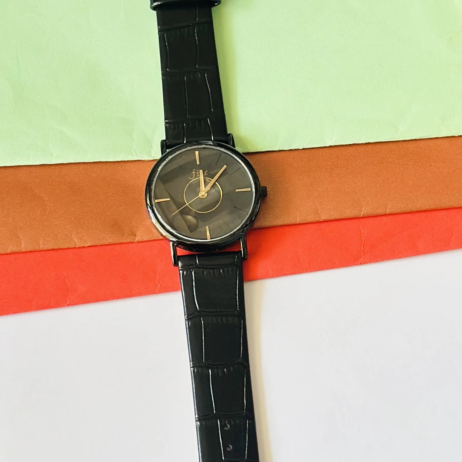 Black analog watch with a black textured leather-style strap.
