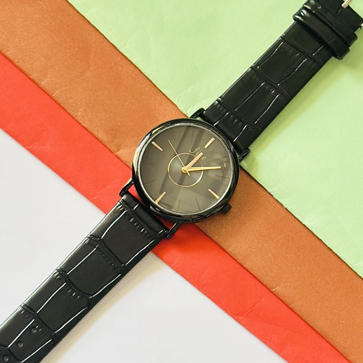 Black analog watch with a black textured leather-style strap.