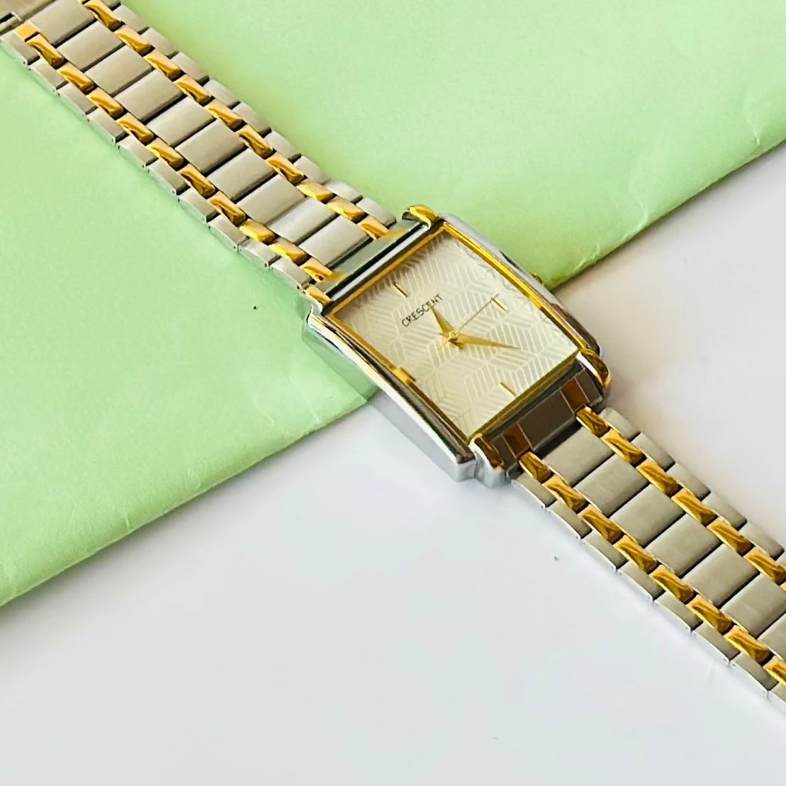 Crescent analog watch with a rectangular case and a two-tone (silver and gold) metal bracelet.