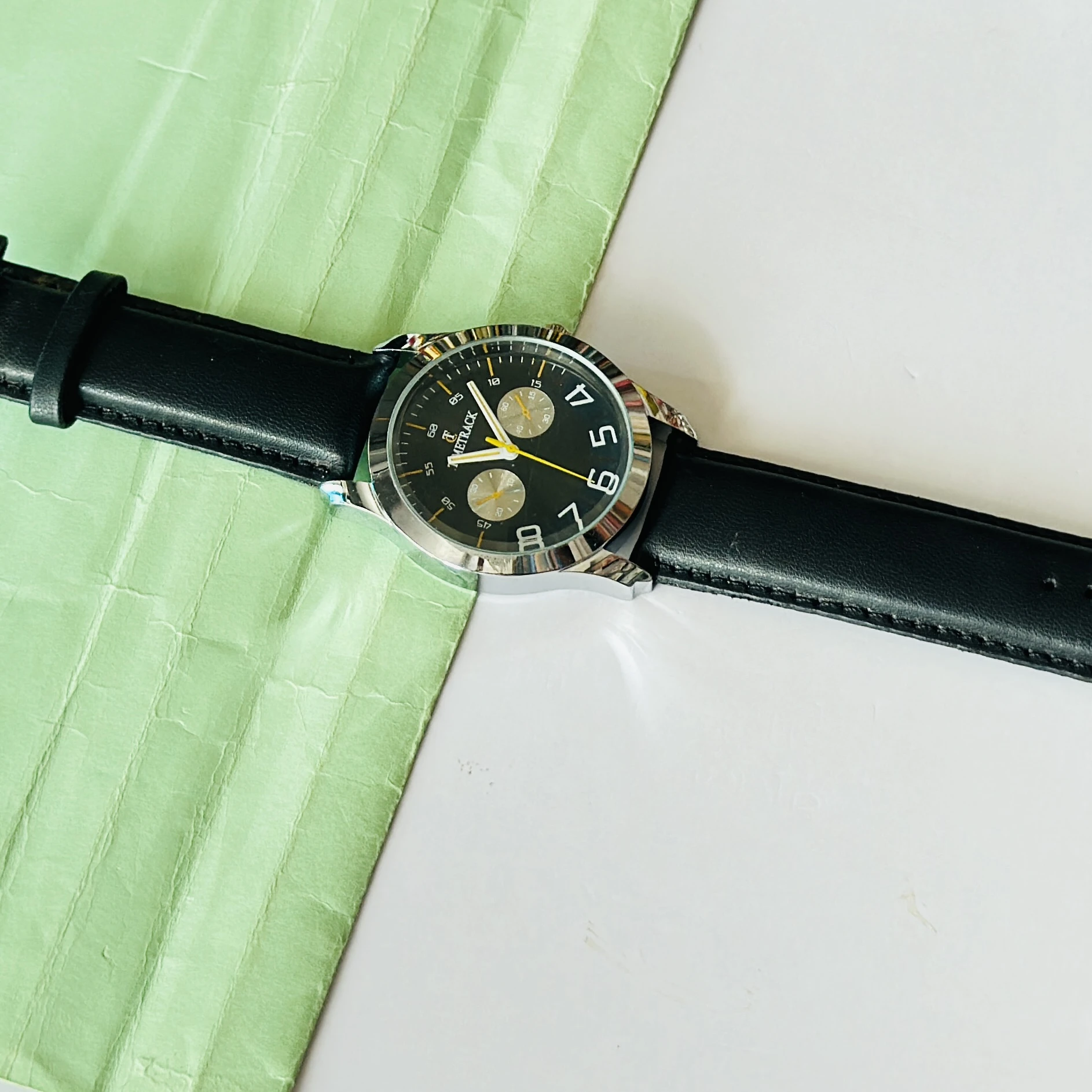Metrack brand analog watch featuring a black dial and a black leather strap.