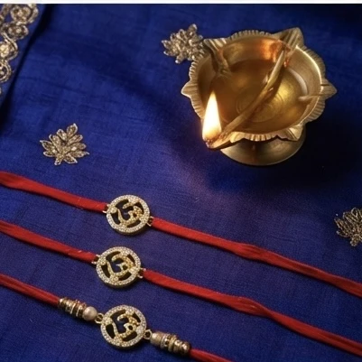 Silver Om-themed rakhis, featuring gold plating and stone studding.
