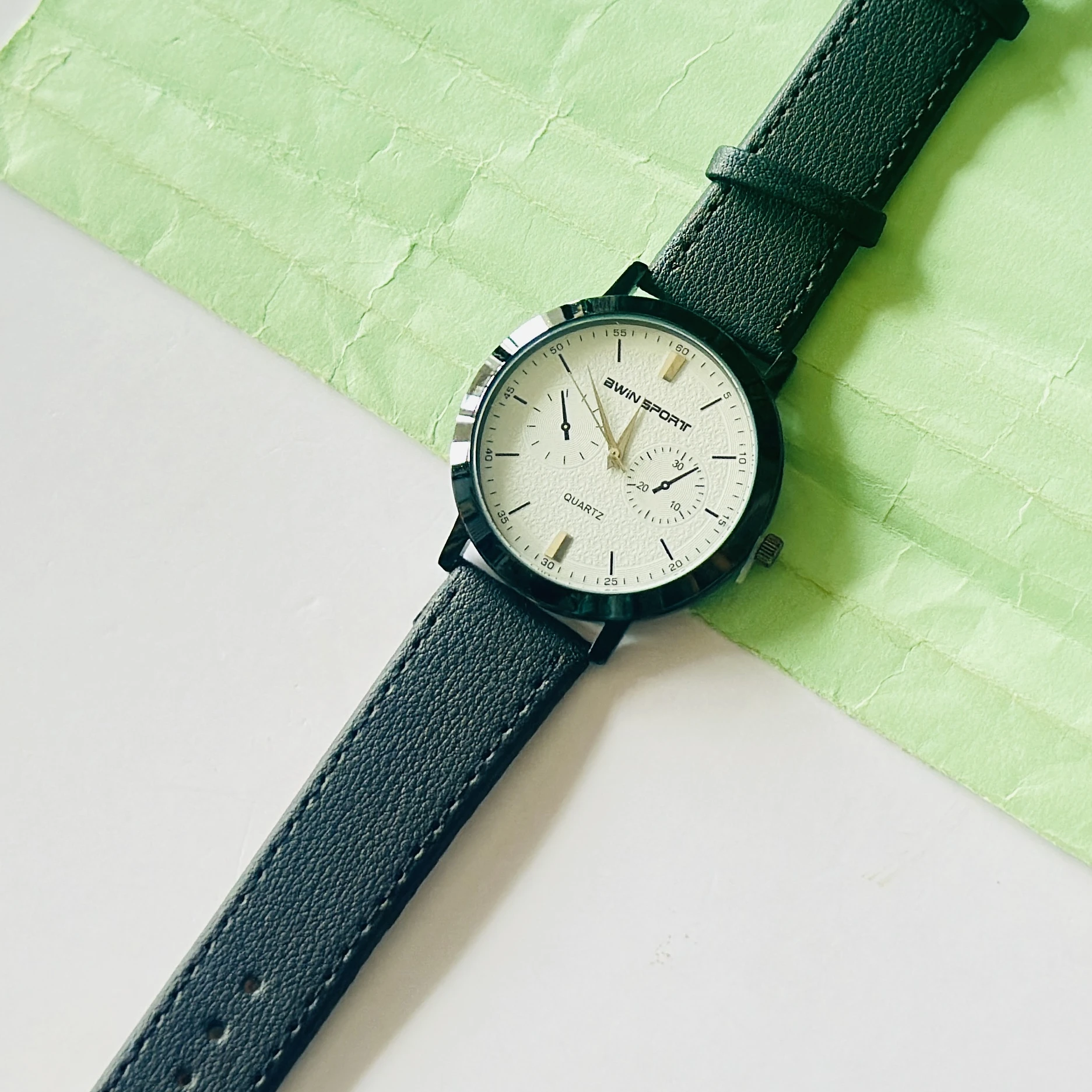 Quartz’s wristwatch featuring a white dial, black markers, and a matching black leather strap.