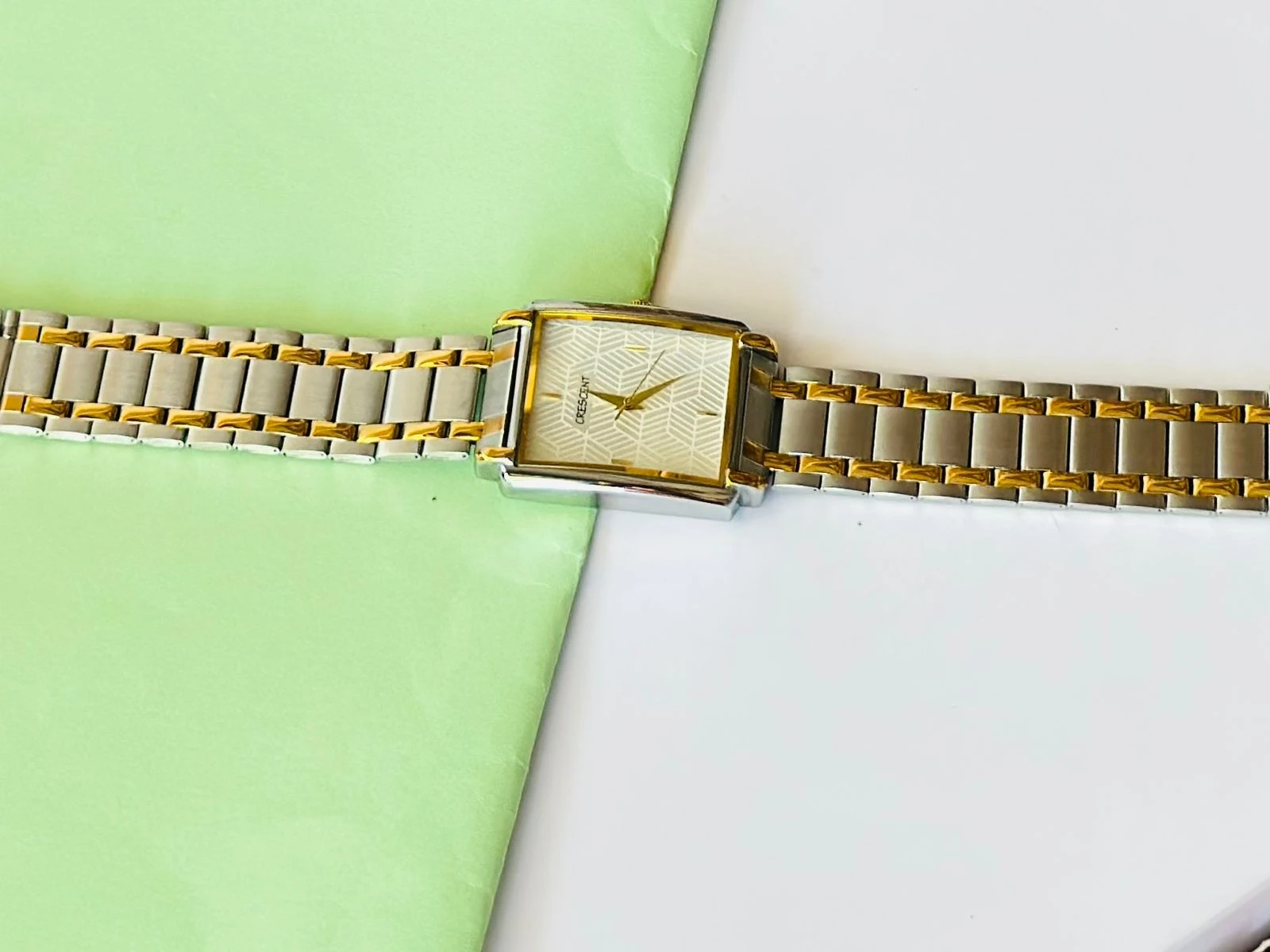 Crescent analog watch with a rectangular case and a two-tone (silver and gold) metal bracelet.