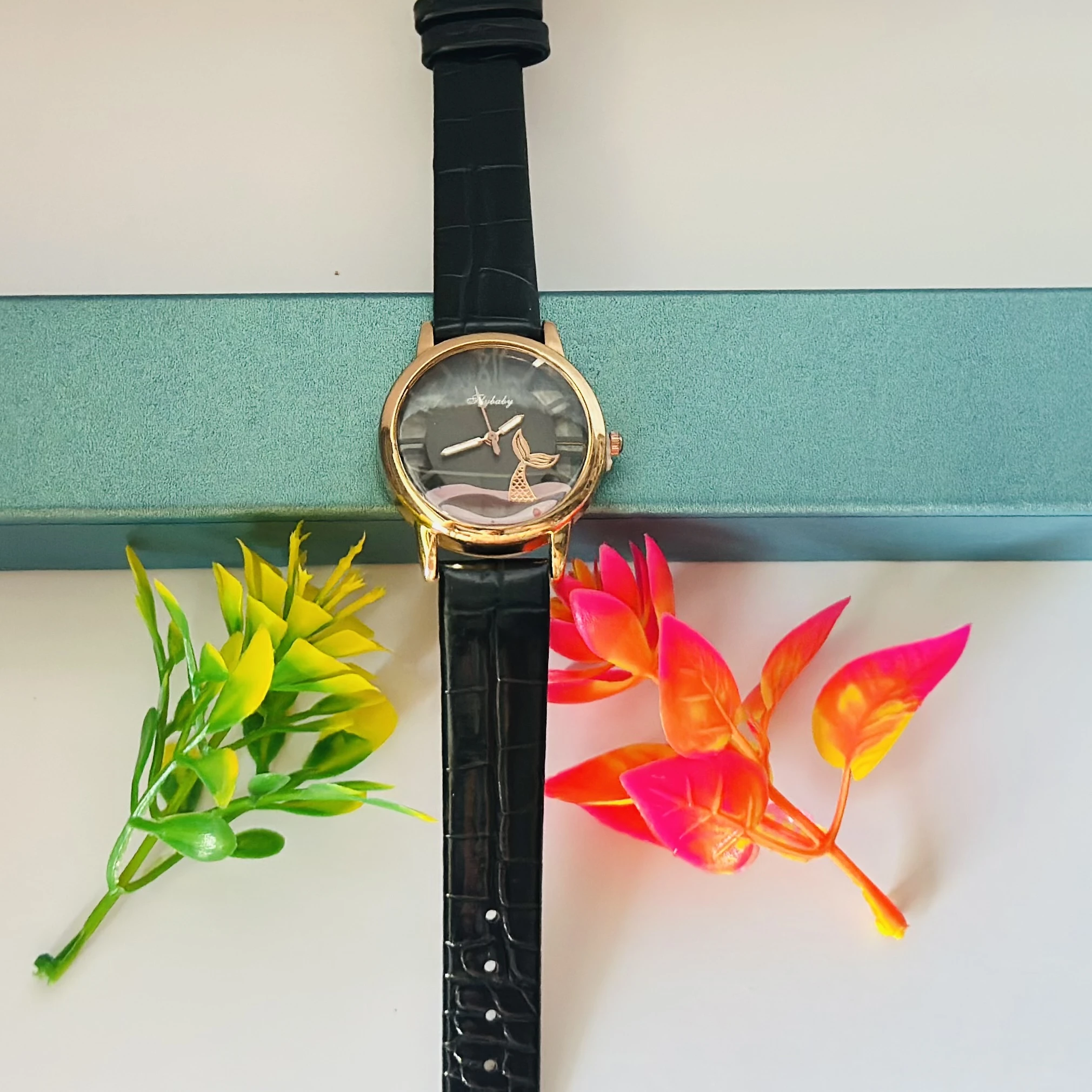 gold-toned analog watch with a black strap and a whale tail design on the dial.