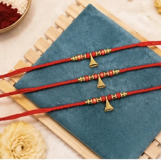 Rakhi  feature a design with small gold-colored beads, red beads, and a central jhumka-style charm on a red thread.