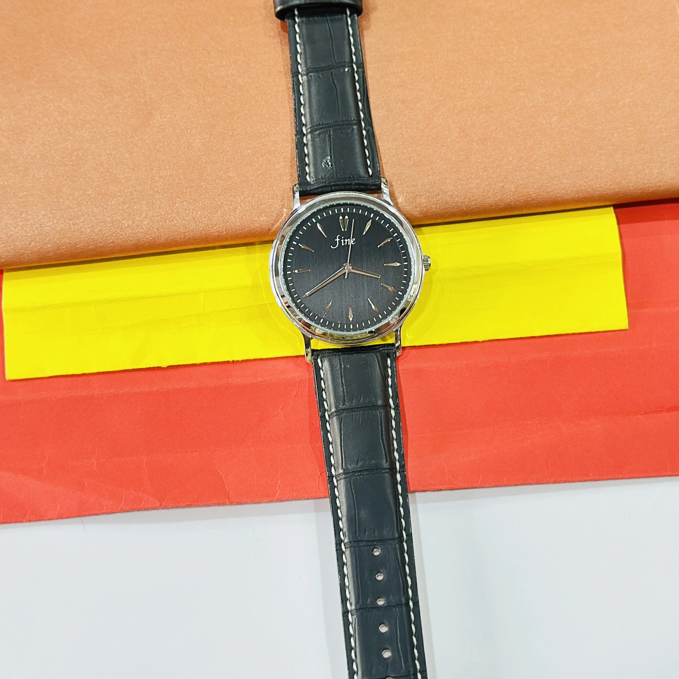wrist watch featuring a black dial branded as "fine" and a black leather strap.