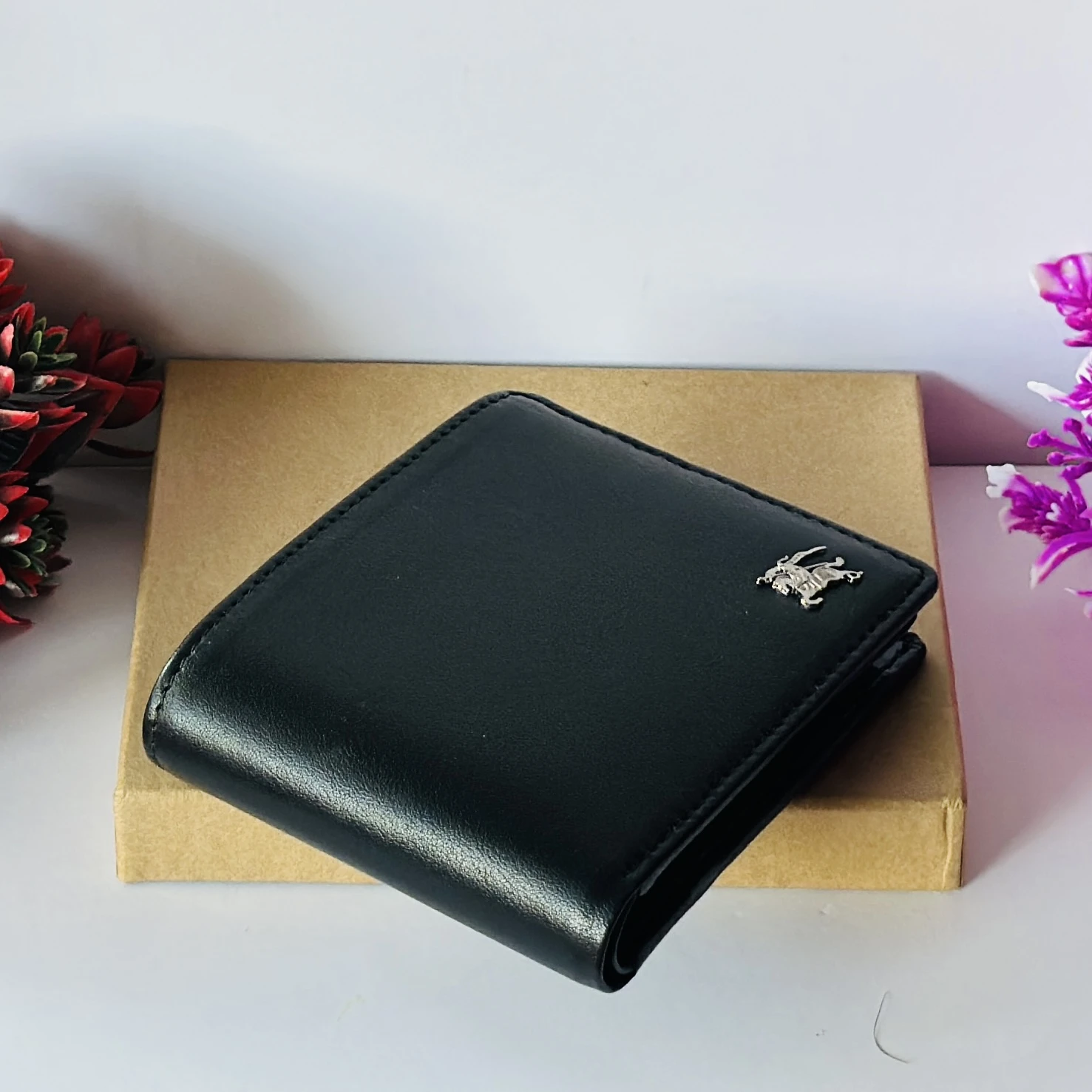 Black bifold leather wallet with a metal logo accent.