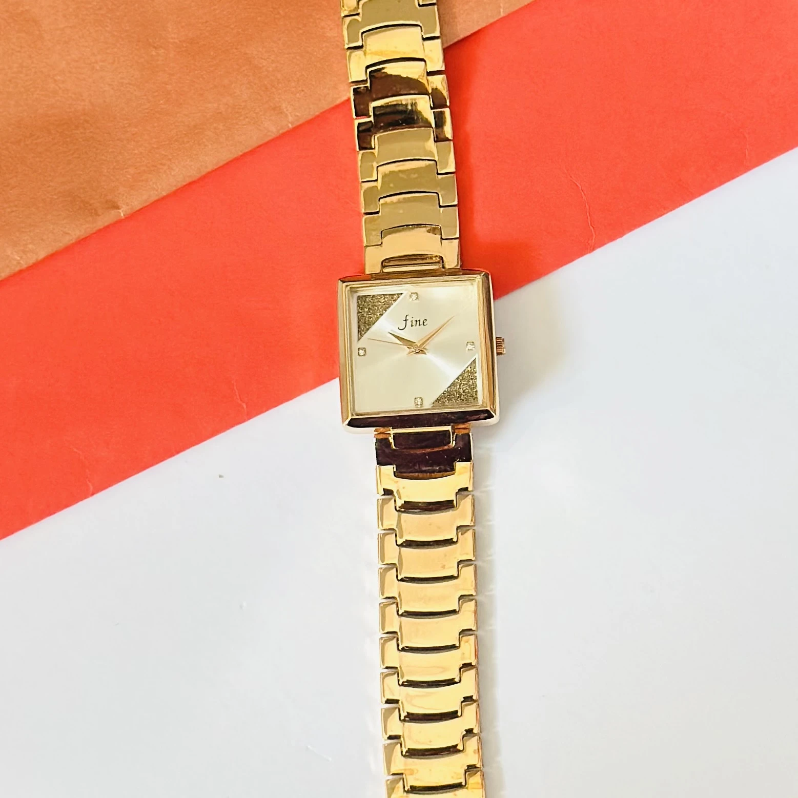 Gold -tone analog watch with a square dial and a metal strap.