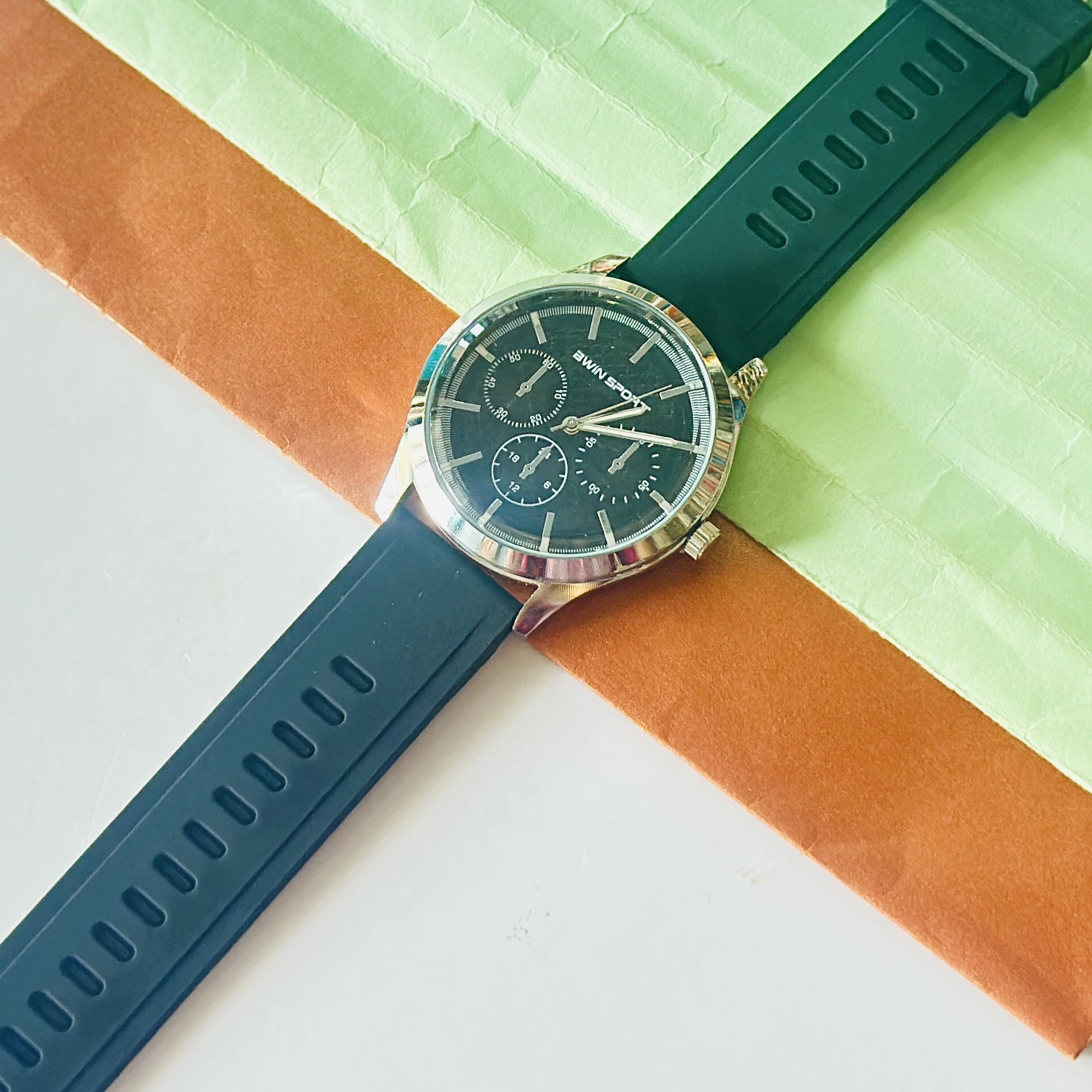 watch features a black dial with sub-dials and a green silicone strap.