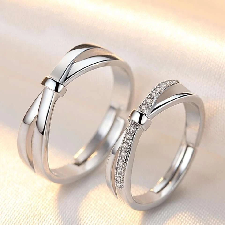 set of silver-plated, adjustable couple rings featuring a double bowknot design, with one ring studded with cubic zirconia stones.