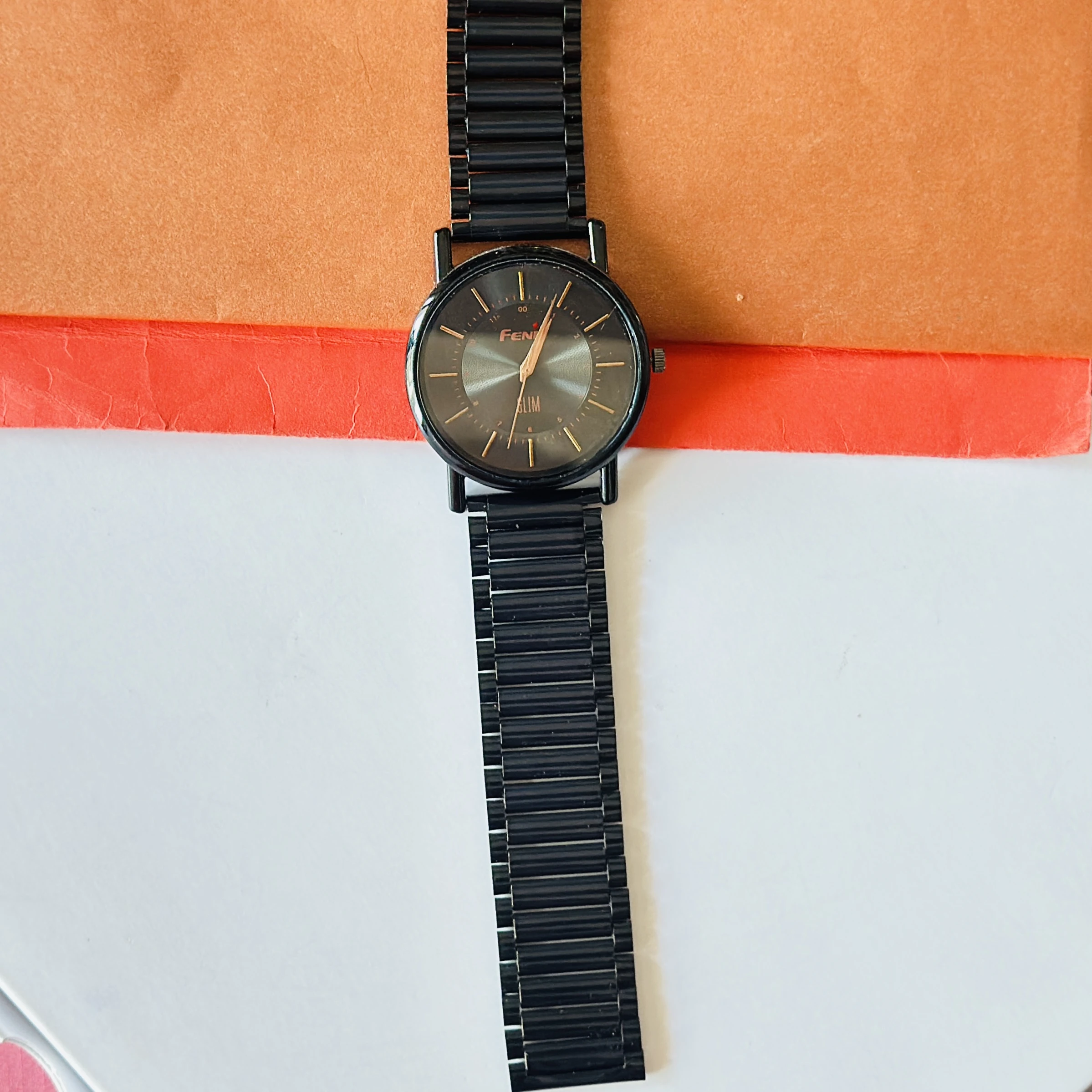 Black metal analog watch with a minimalist design and thin bracelet strap.