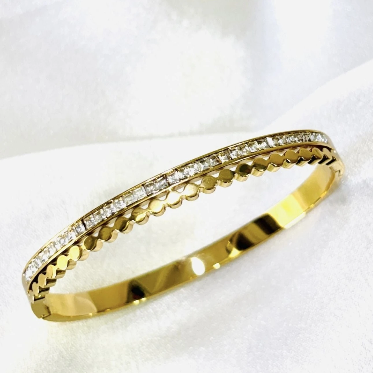 gold-plated stainless steel design with a row of clear stone accents and a scalloped edge.