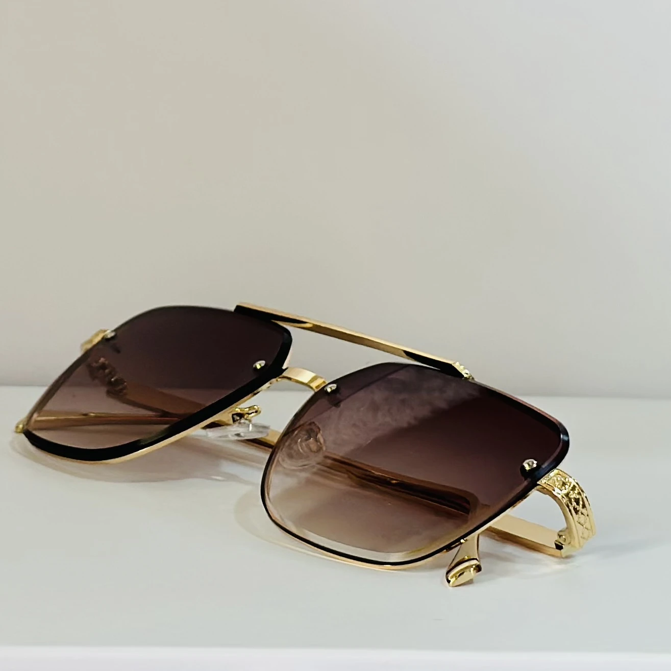 pair of rimless gradient brown aviator sunglasses with a gold metal frame and ornate side details.