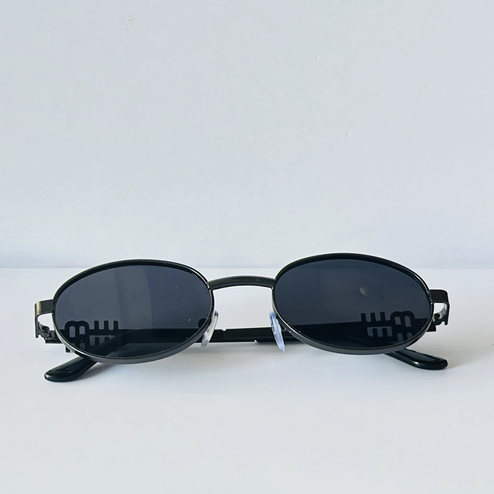 sunglasses featuring a distinct black oval frame and small logo detailing on the lenses