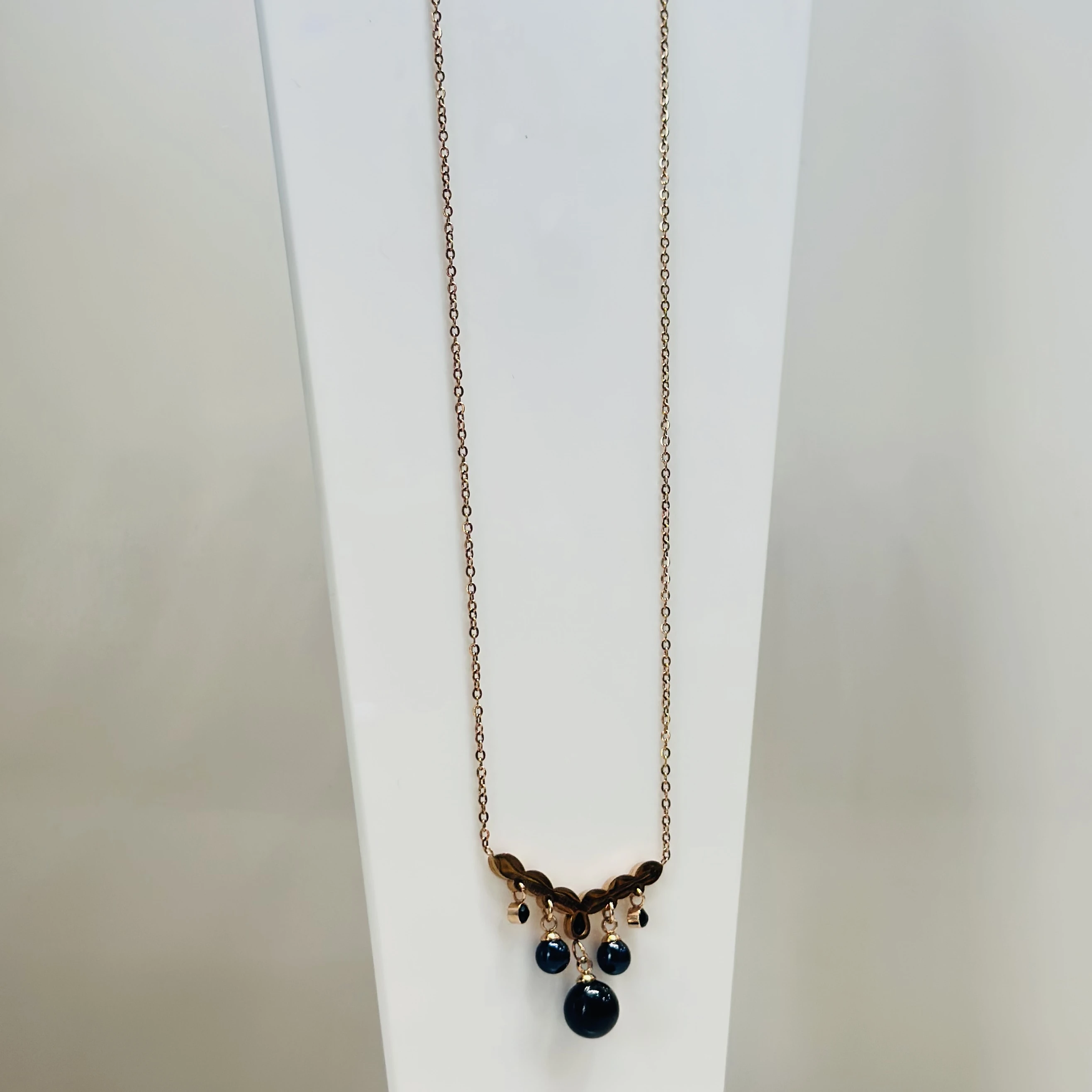 Rose gold-plated pendant necklace with a leaf-motif pendant and black beads.