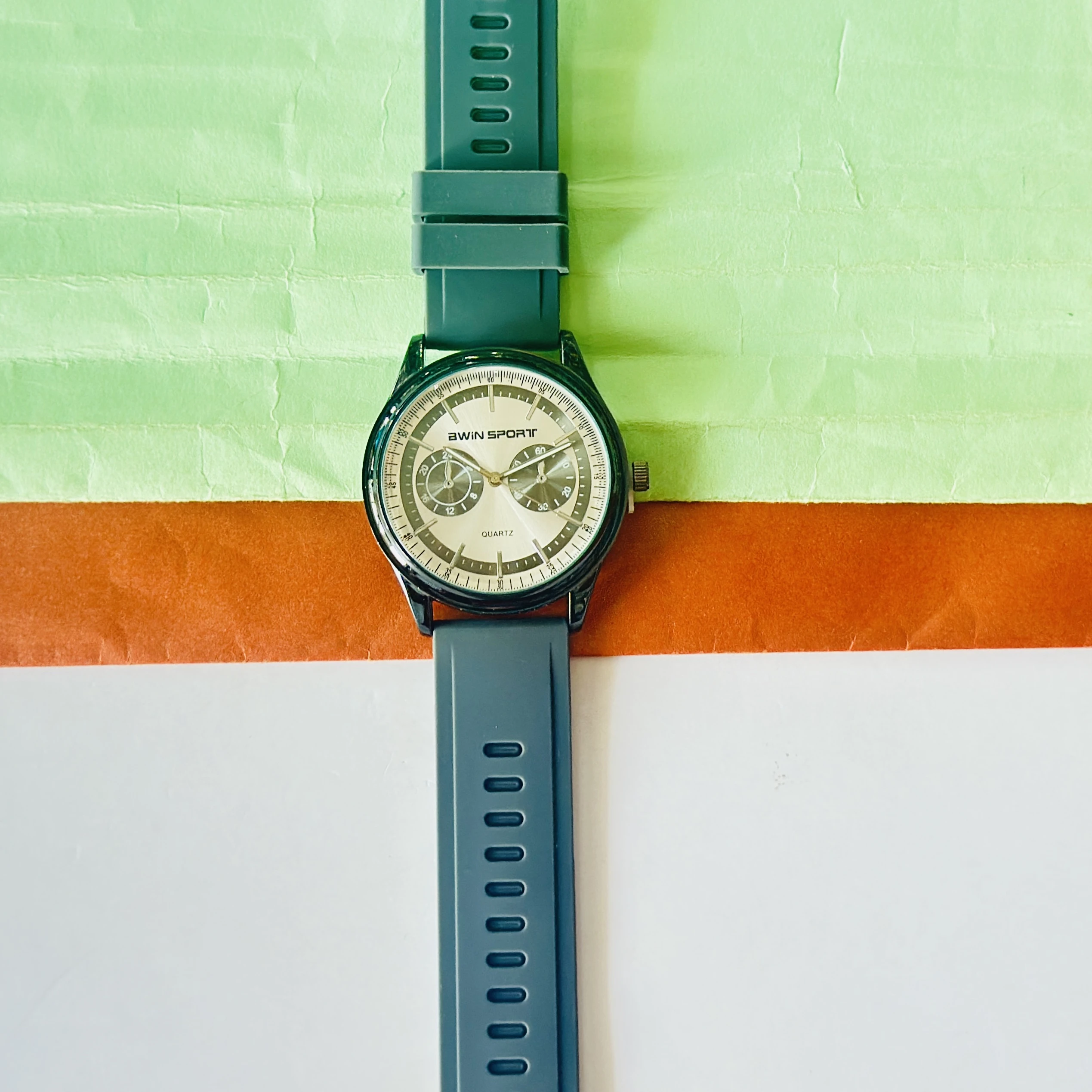 watch features a black dial with sub-dials and a green silicone strap.