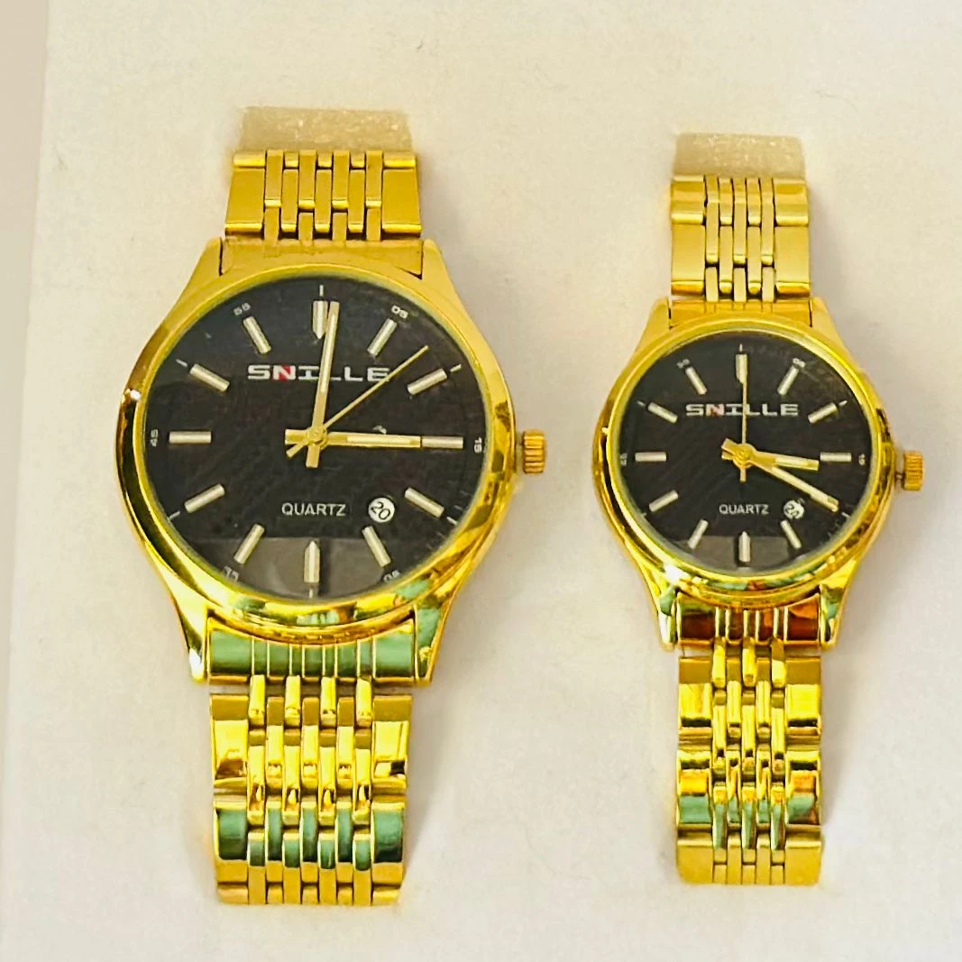 pair of Snille Date Series analog quartz watches for men and women with gold-tone link bracelets and black dials.